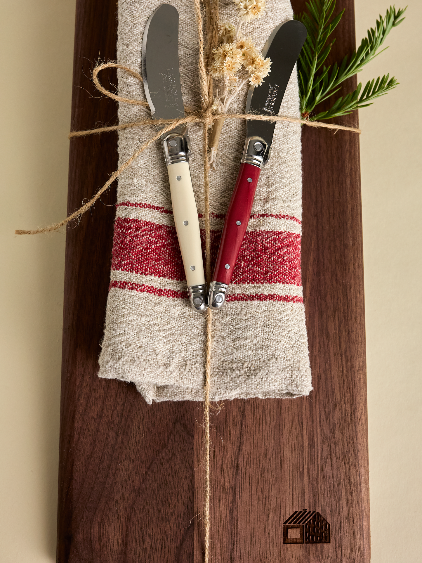 Neutral and red striped fabric napkin with red and creme cheese knives on top of domecíl Walnut Cutting Board