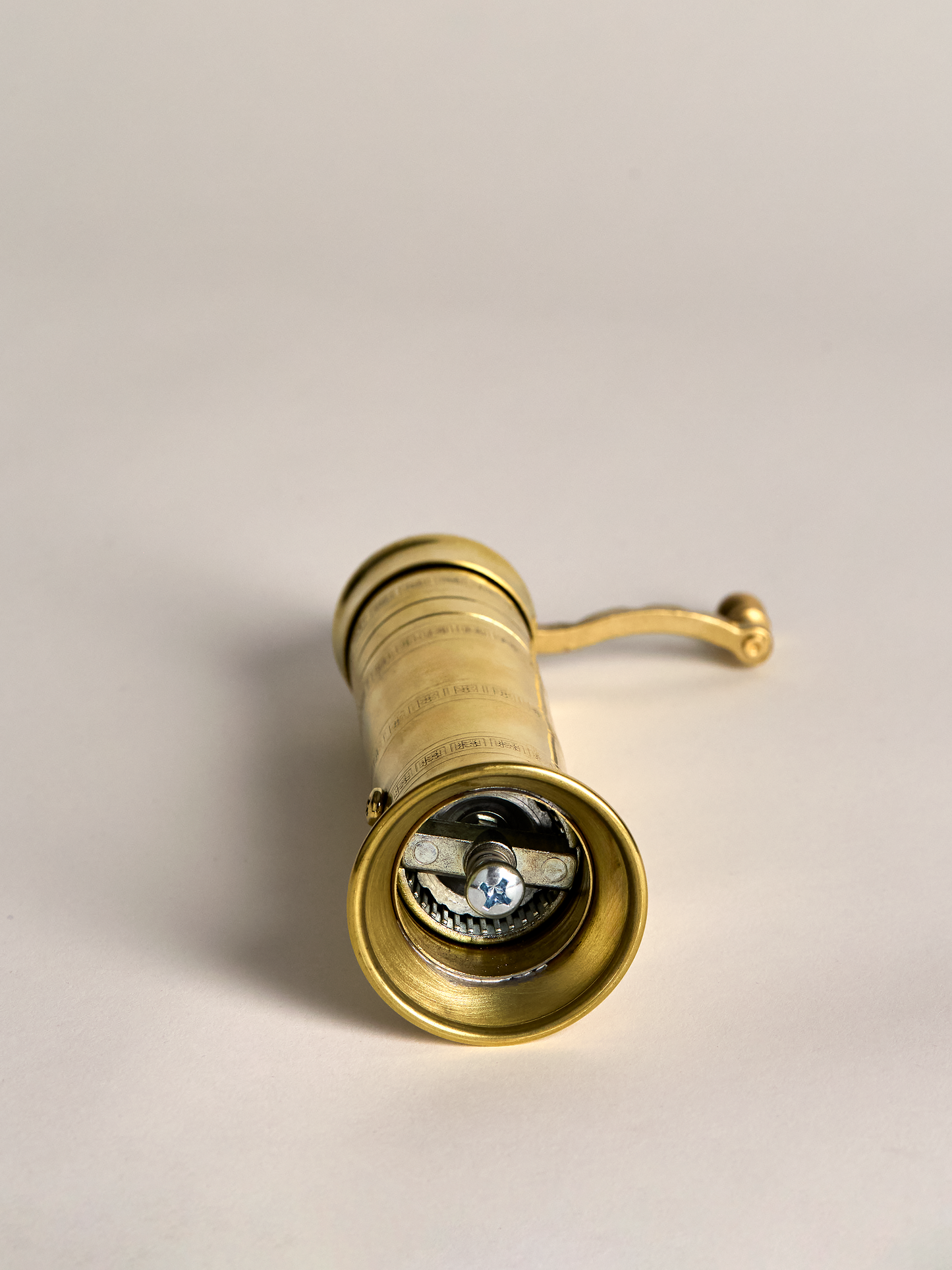 Brass pepper grinder end view on a light gray background