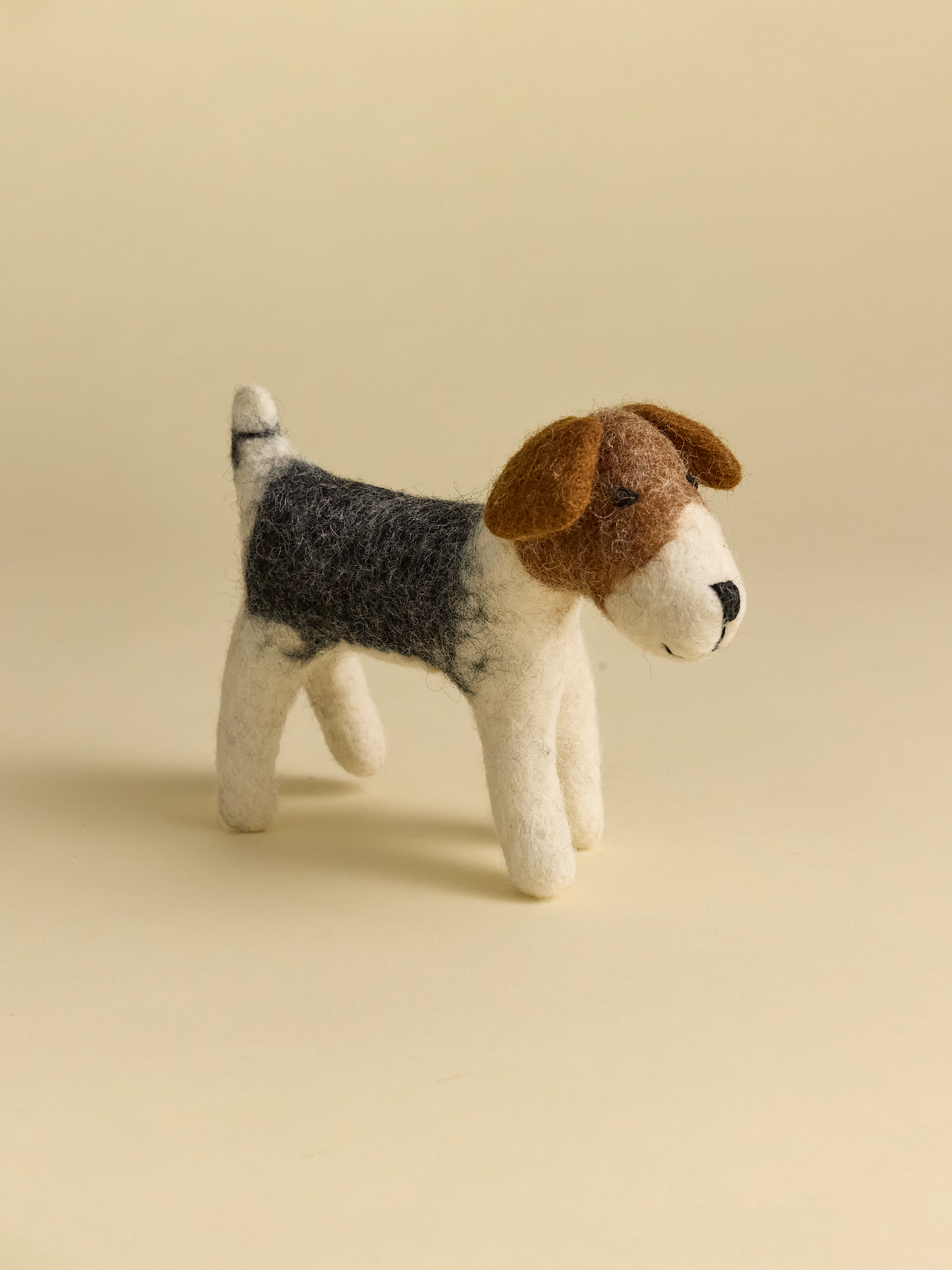 Alternate side view of small felt dog on neutral background with gray and brown features