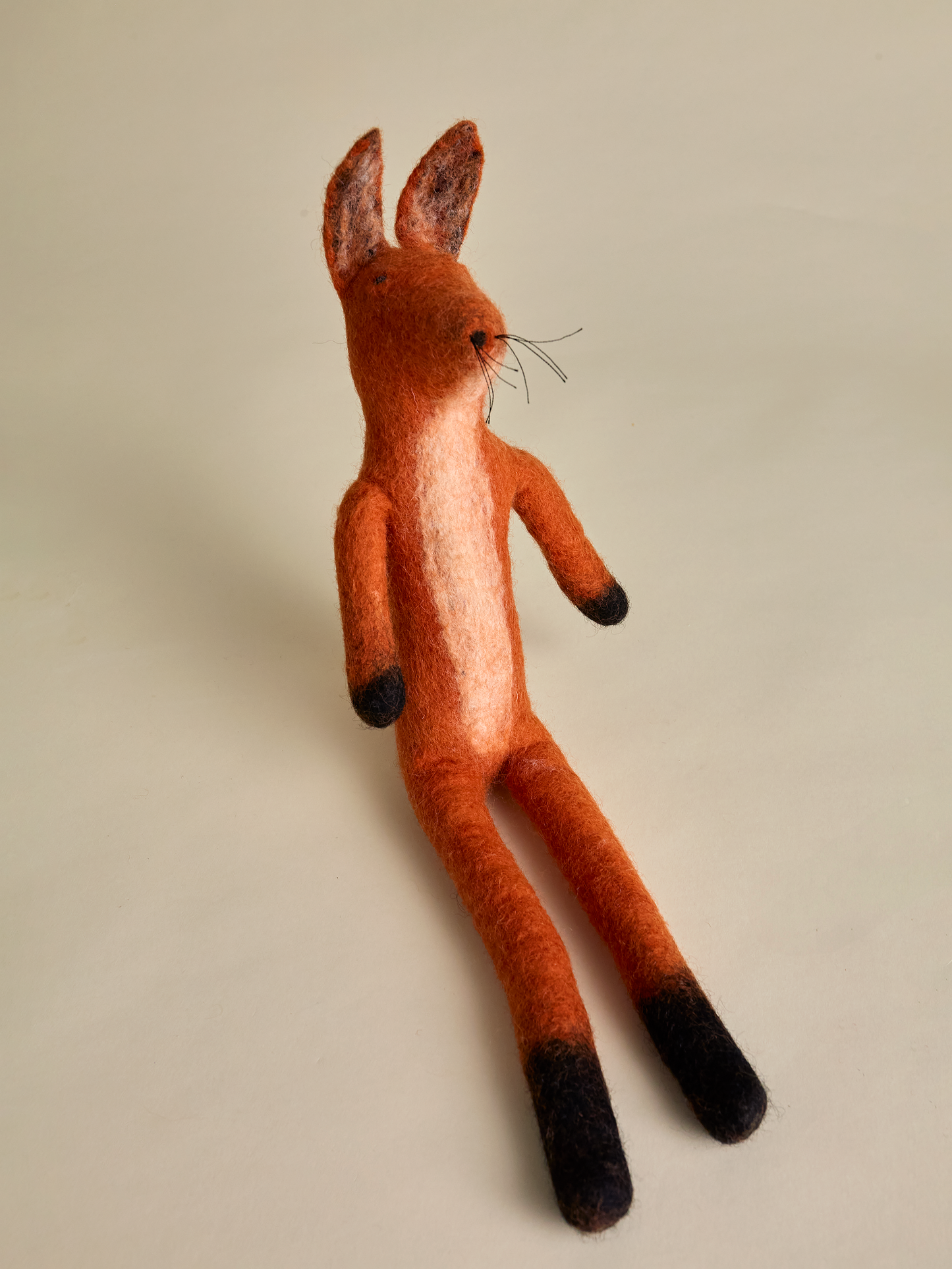 Orange felt fox sitting upright on neutral background