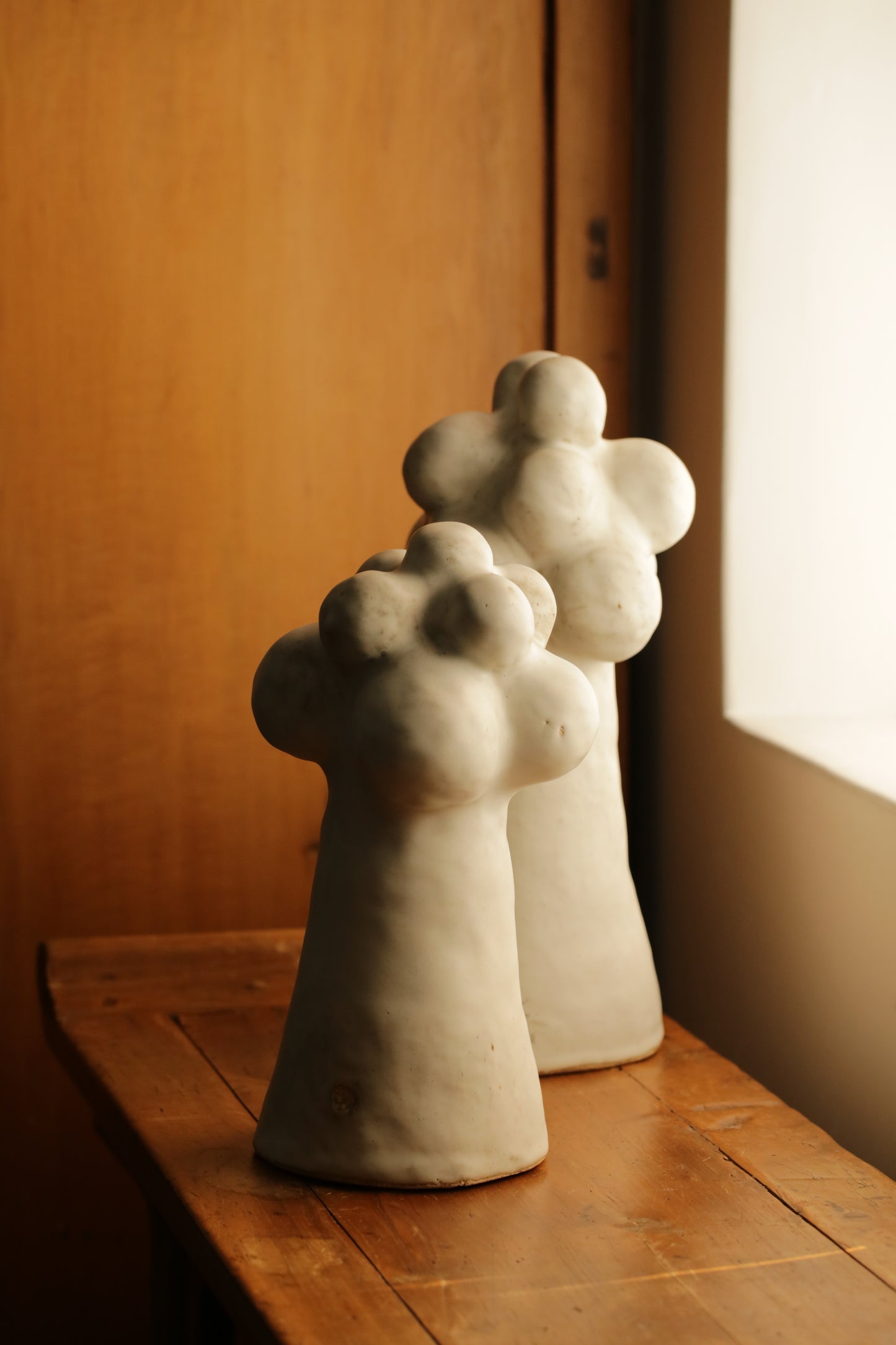 Two Pascale Vaqutte ceramic matte glaze Cloud  Sculptures against a wooden and beige background