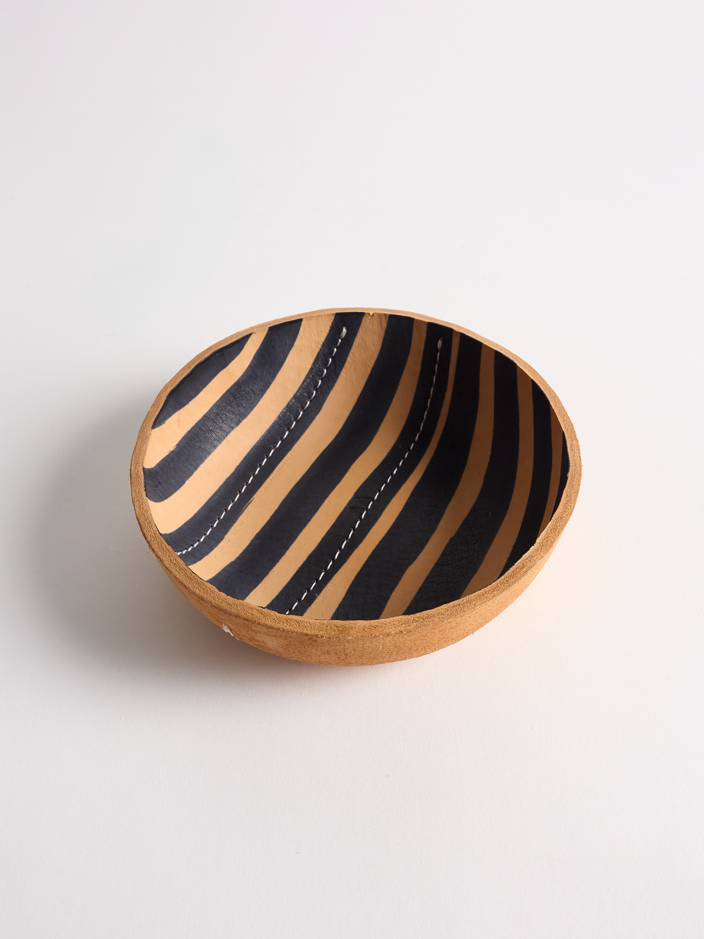 Leather bowl with black stripes and white stitching on a light gray background