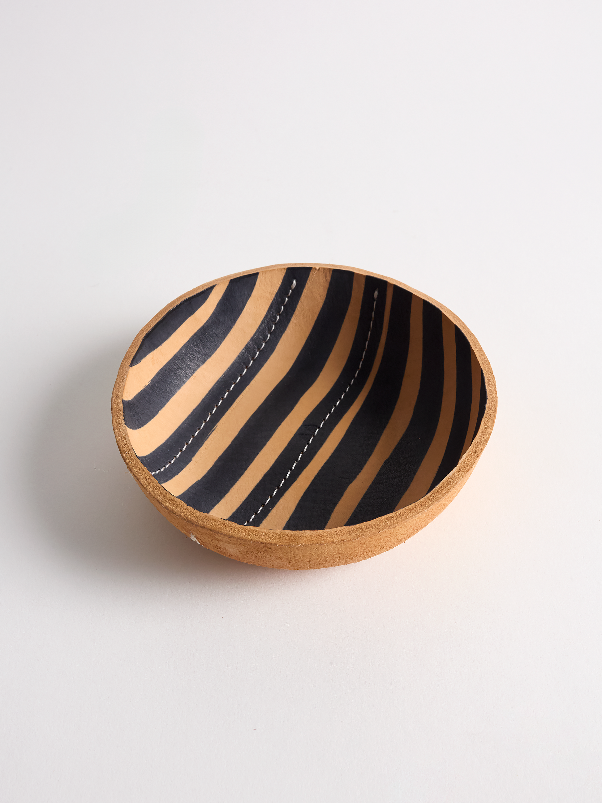 Leather bowl with black stripes and white stitching on a light gray background