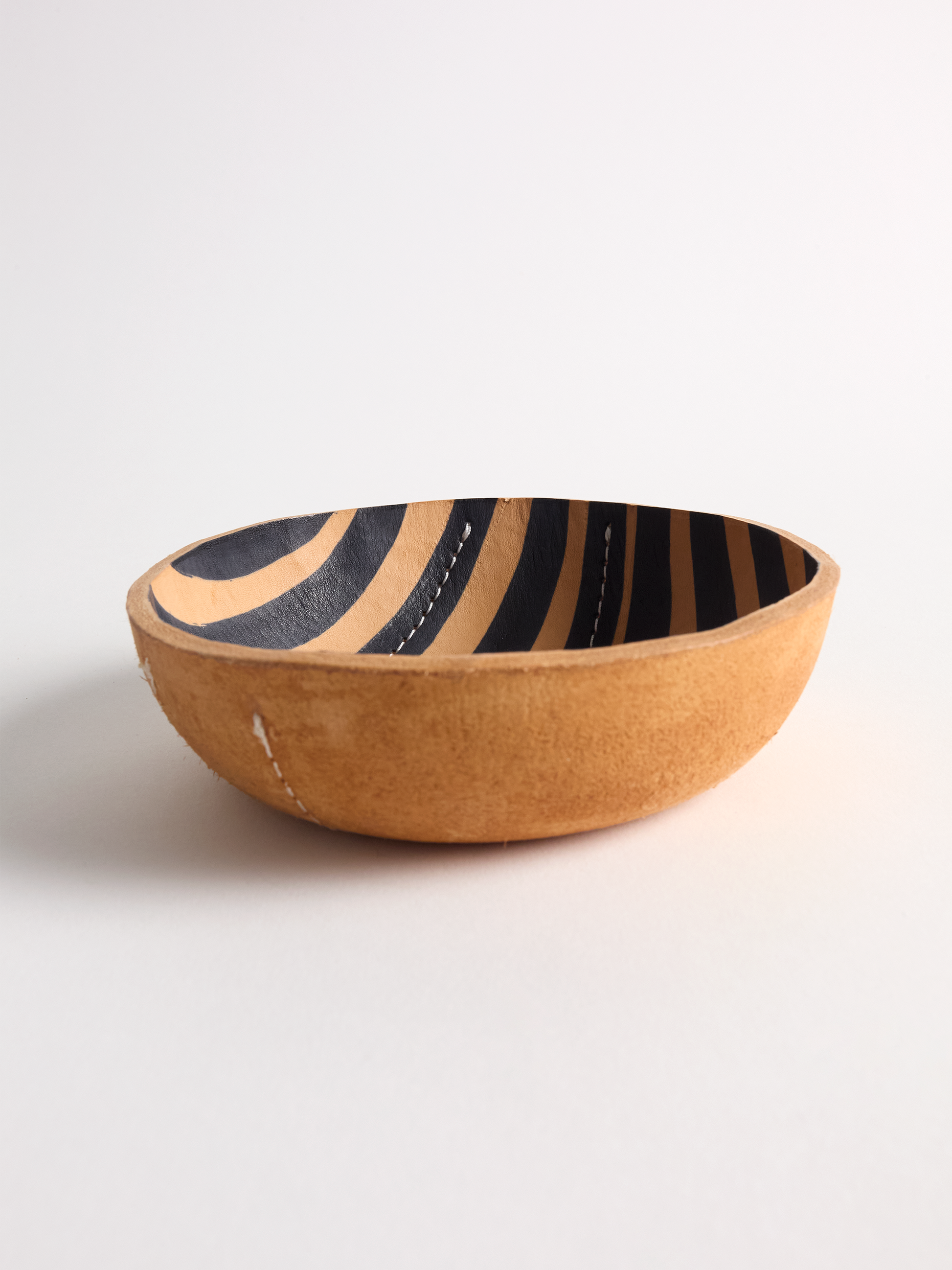 Leather bowl with black striped  interior on a light background