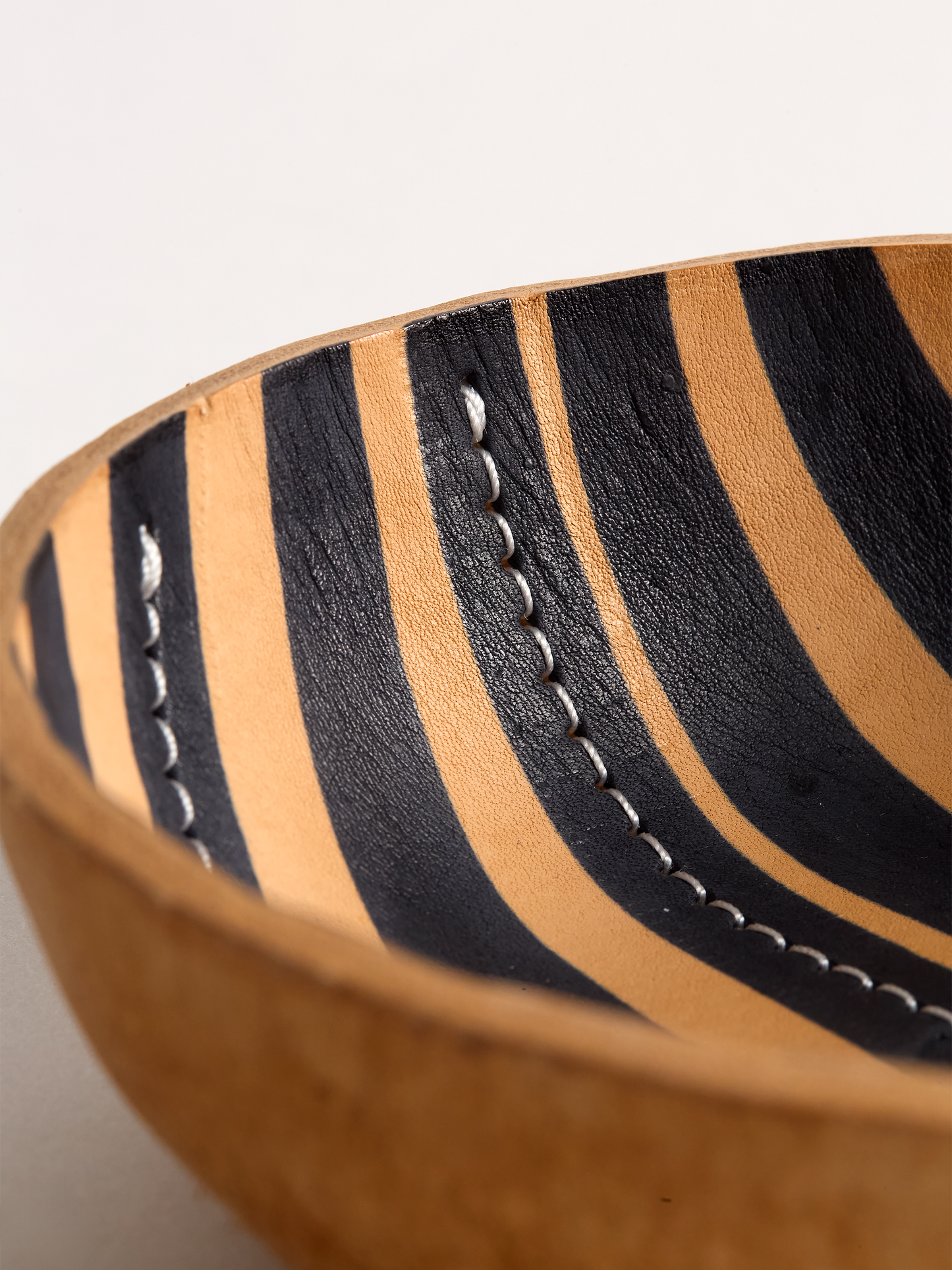 Close Up angle of a Brown leather bowl with black stripe on a light gray background showing detail