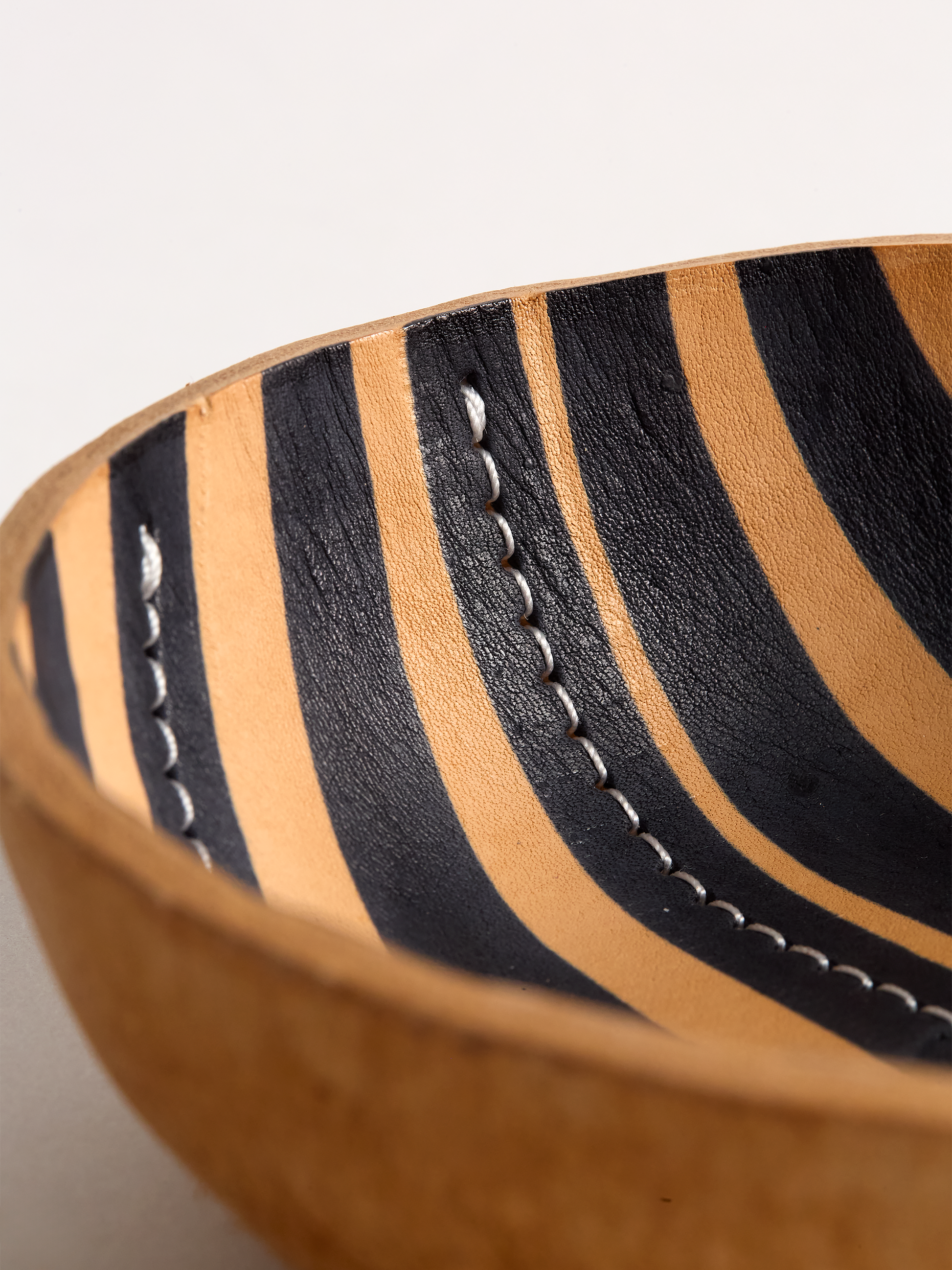 Close Up angle of a Brown leather bowl with black stripe on a light gray background showing detail