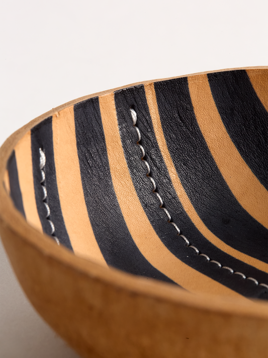 Close Up angle of a Brown leather bowl with black stripe on a light gray background showing detail