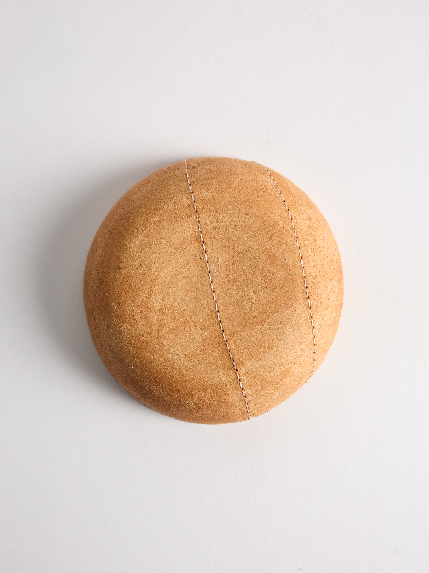 Brown leather bowl bottom with visible stitching on a light background