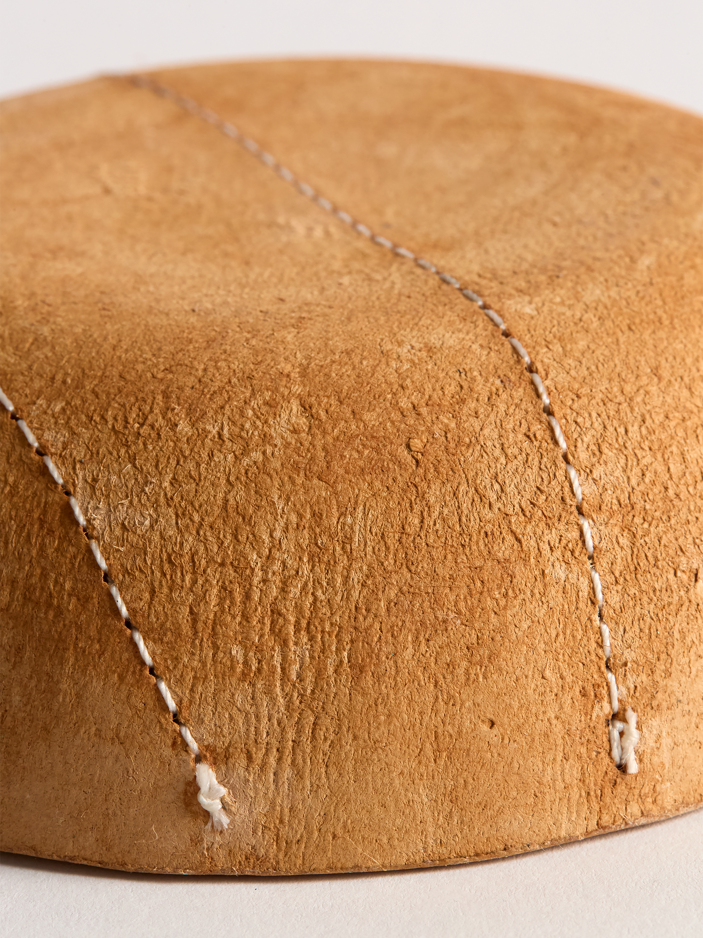 Close-up of light brown leather bowl bottom with visible stitching on a light background