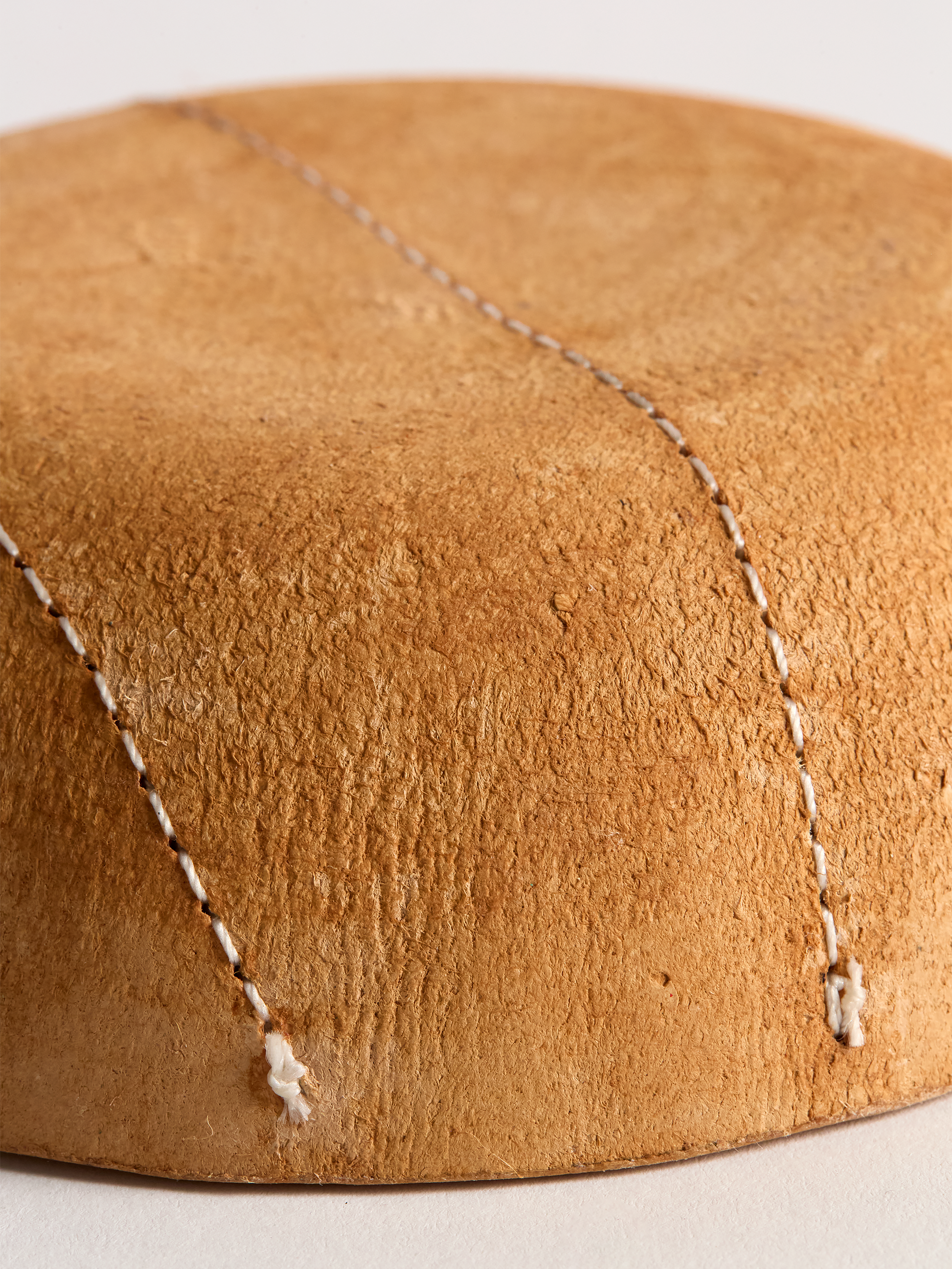 Close-up of light brown leather bowl bottom with visible stitching on a light background