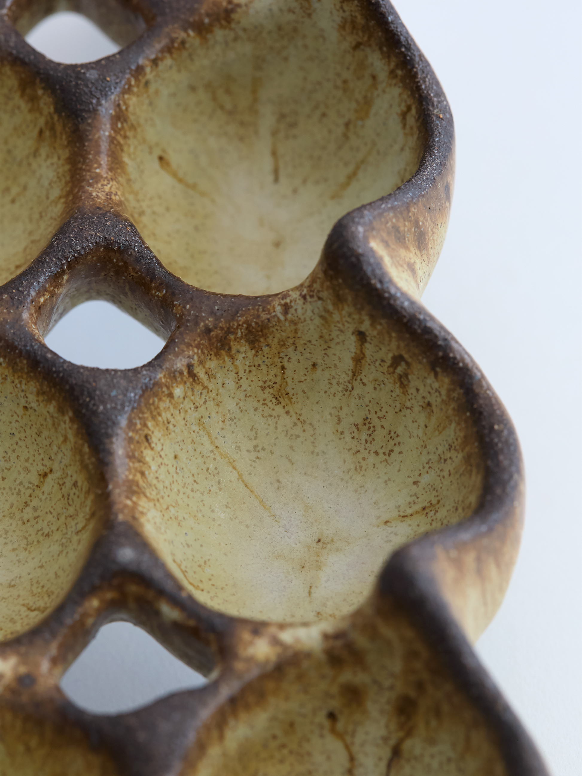 Close-up of a textured ceramic egg holder with brown and beige colors on a white background