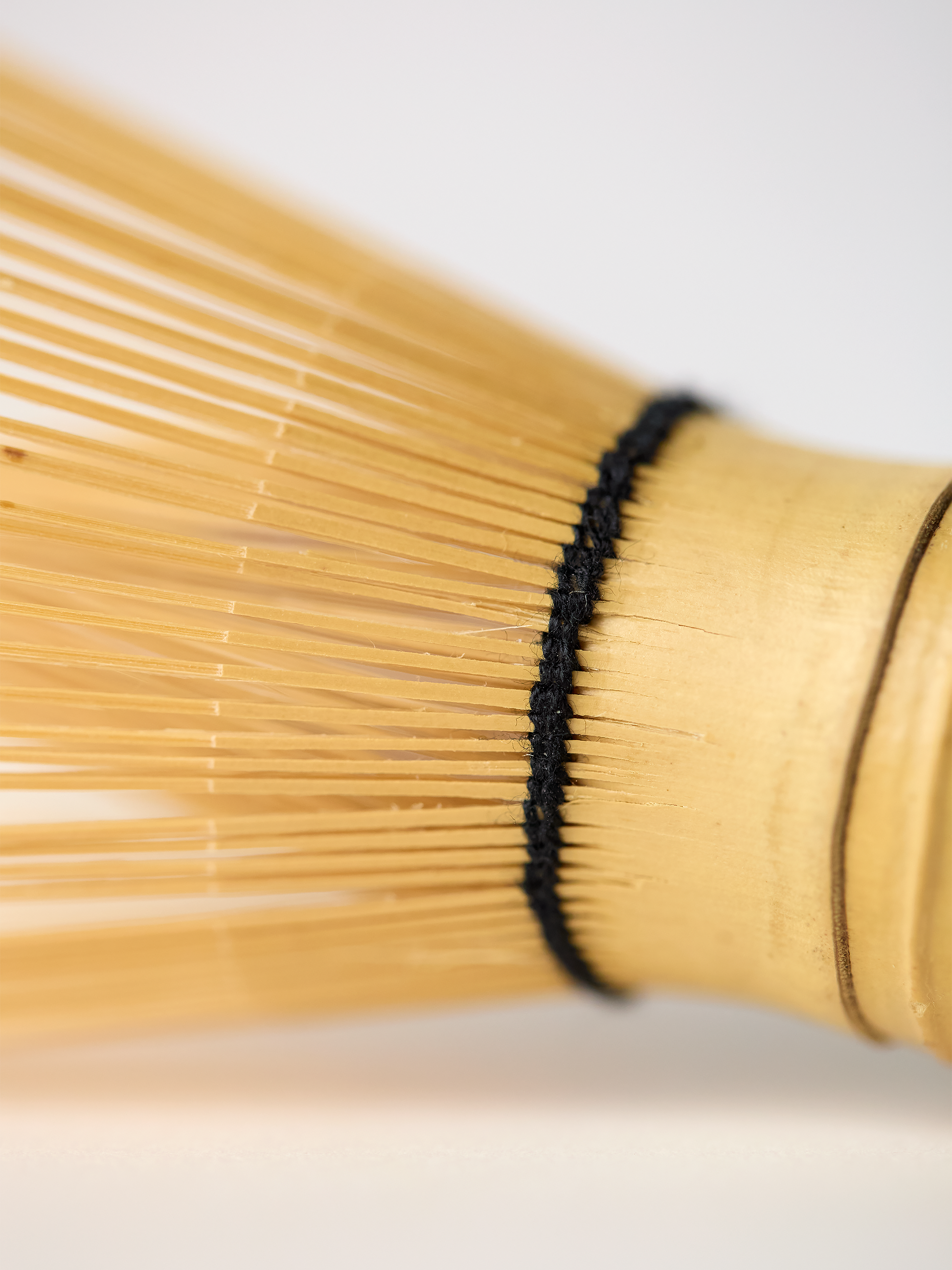 Close-up of a bamboo matcha whisk with a black band on a light background