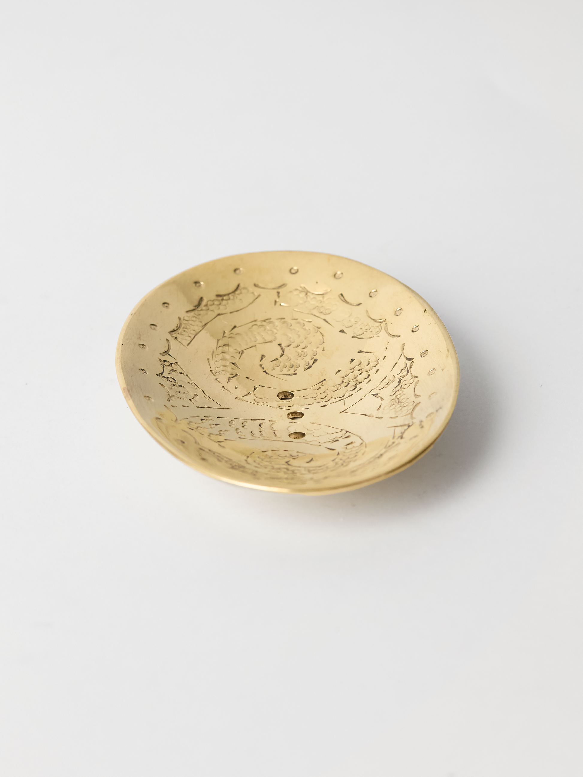unlaquered brass soap dish wit intricate patterns on a white background