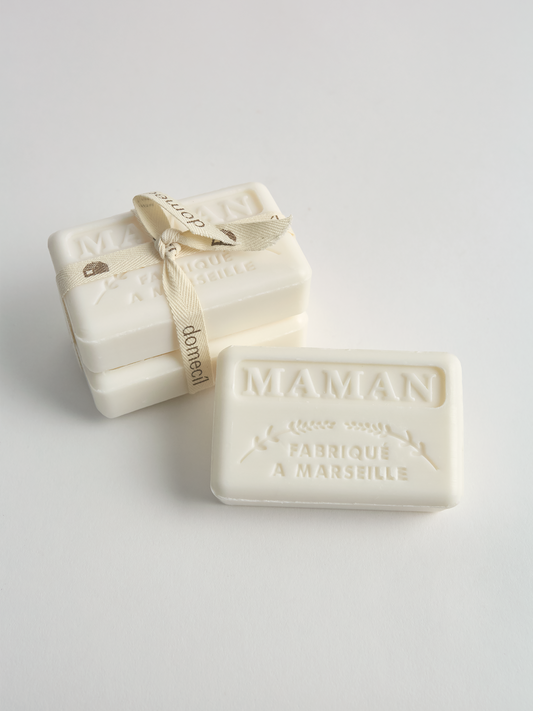 Two bars of soap bundled with 'Domecil' strap with 'MAMAN' branding on a light gray background