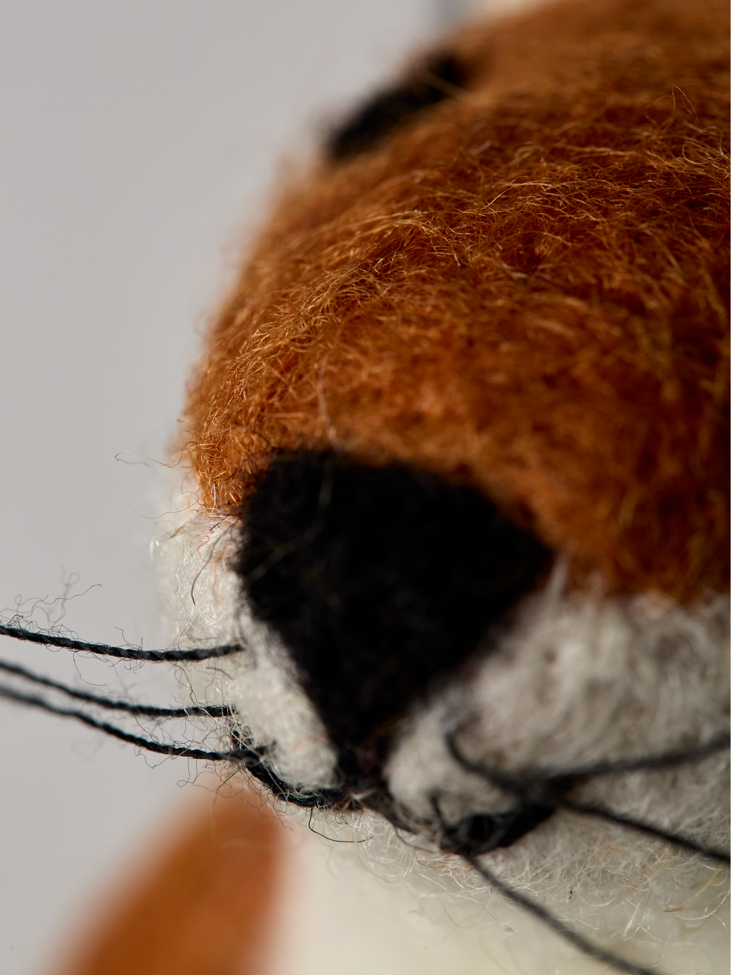 Close-up of a felt fox toy with brown fur, black nose, and white chest on a light gray background.
