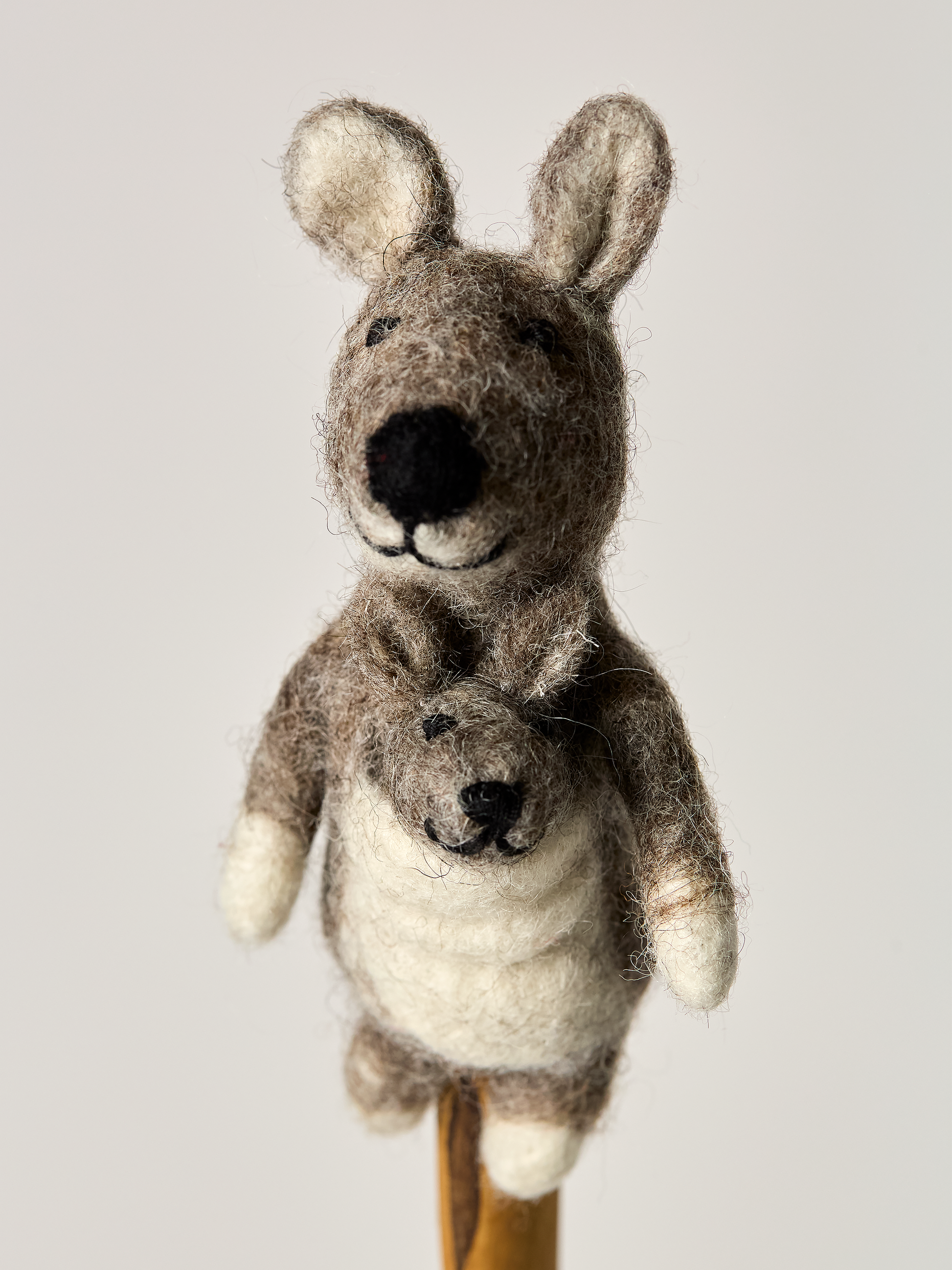 A felt finger puppet gray mother kangaroo and baby on a wooden stick against a light background