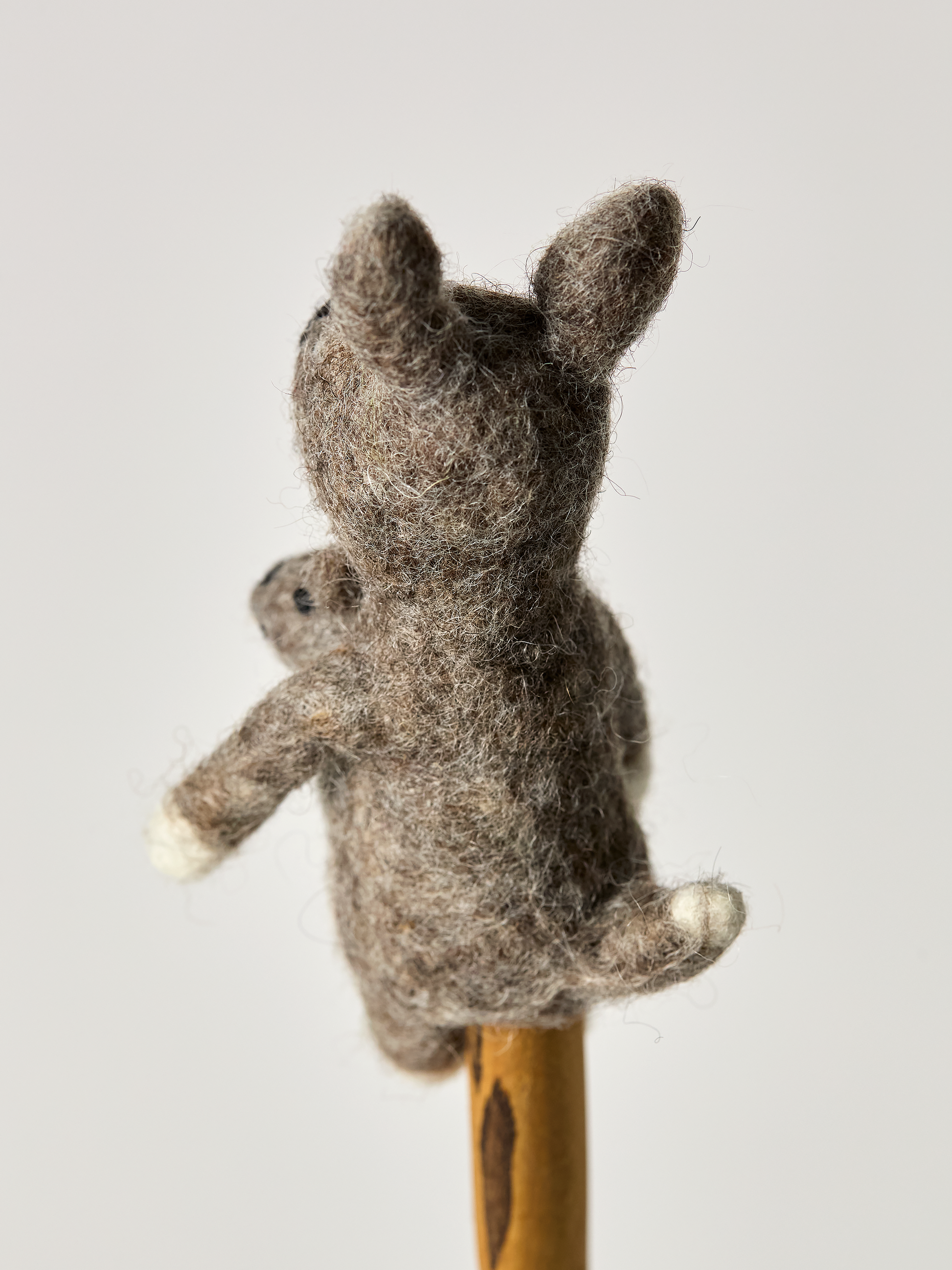 Backside of a felt finger puppet gray kangaroo on a wooden stick against a light background