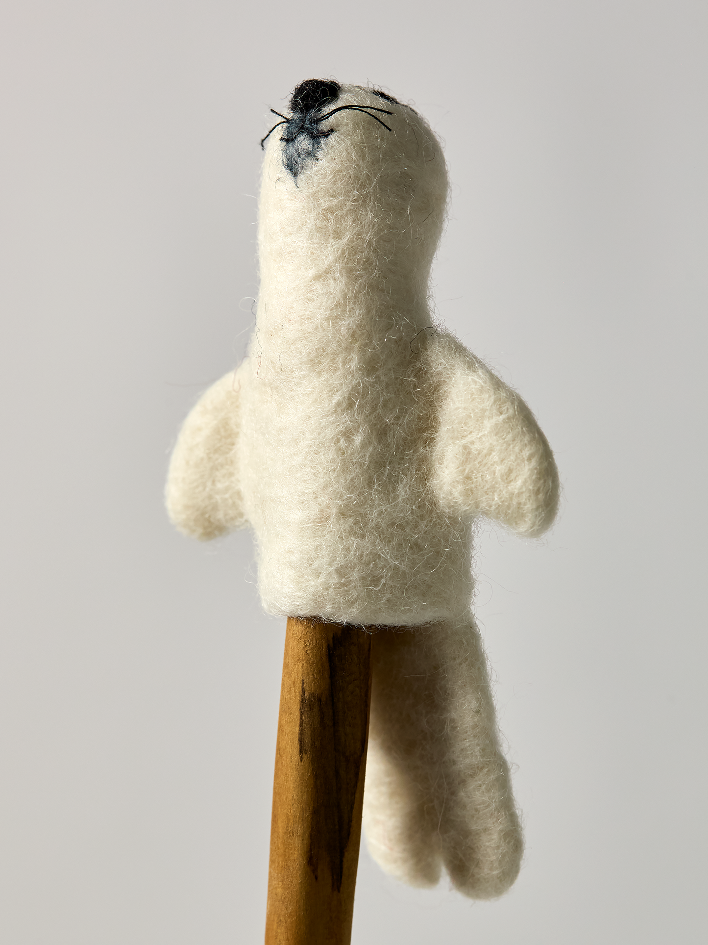White plush Seal finger puppet on a wooden stand against a plain background