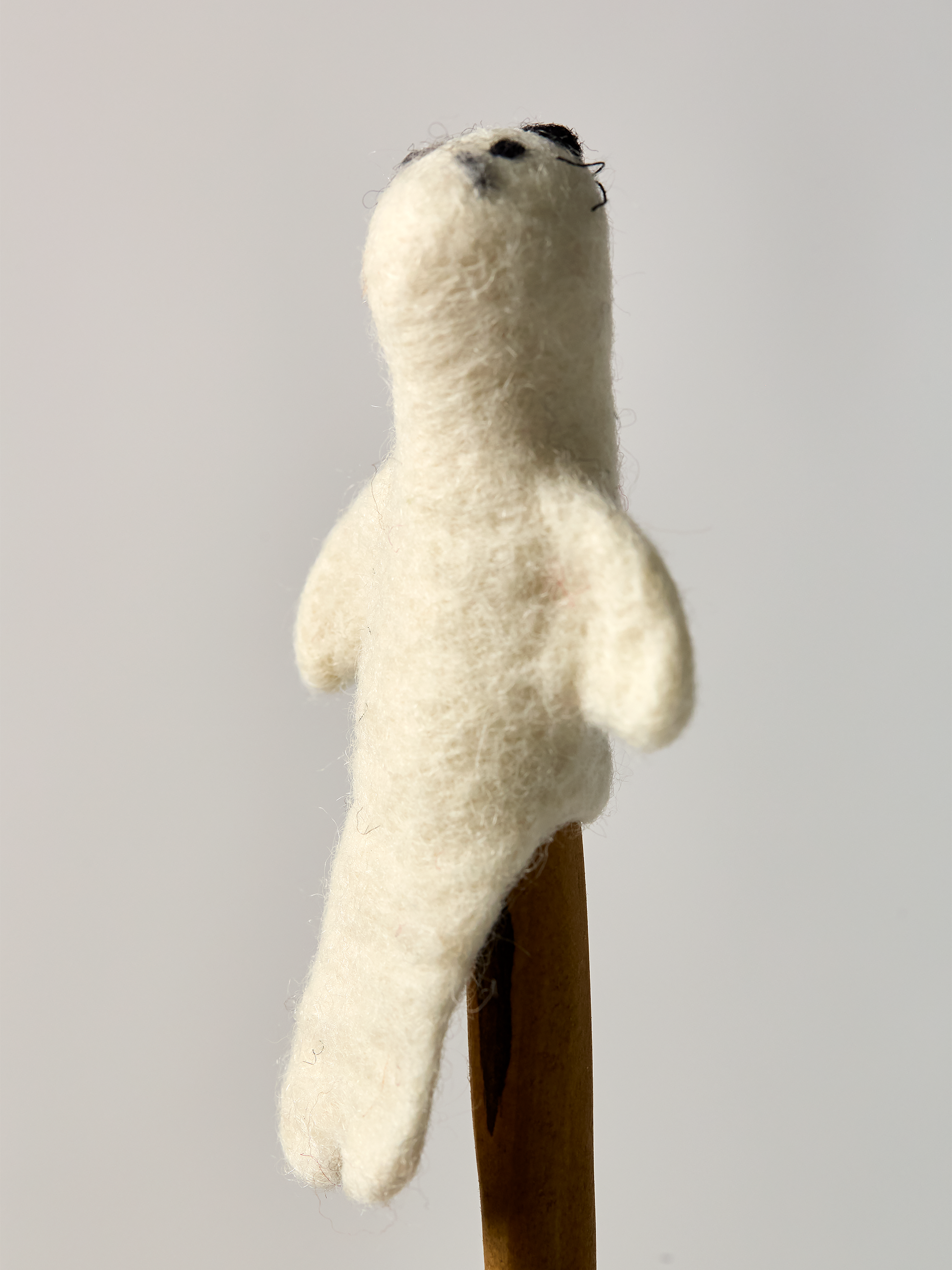 White plush Seal finger puppet back side on a wooden stand against a plain background