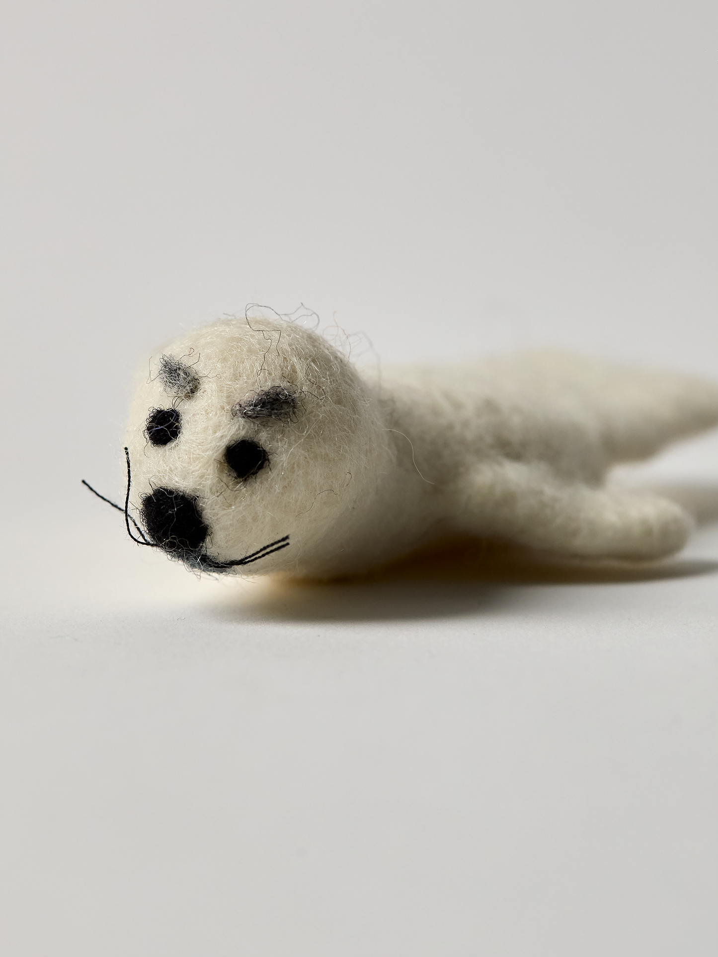 White seal finger puppet with black eye brows on a light gray background