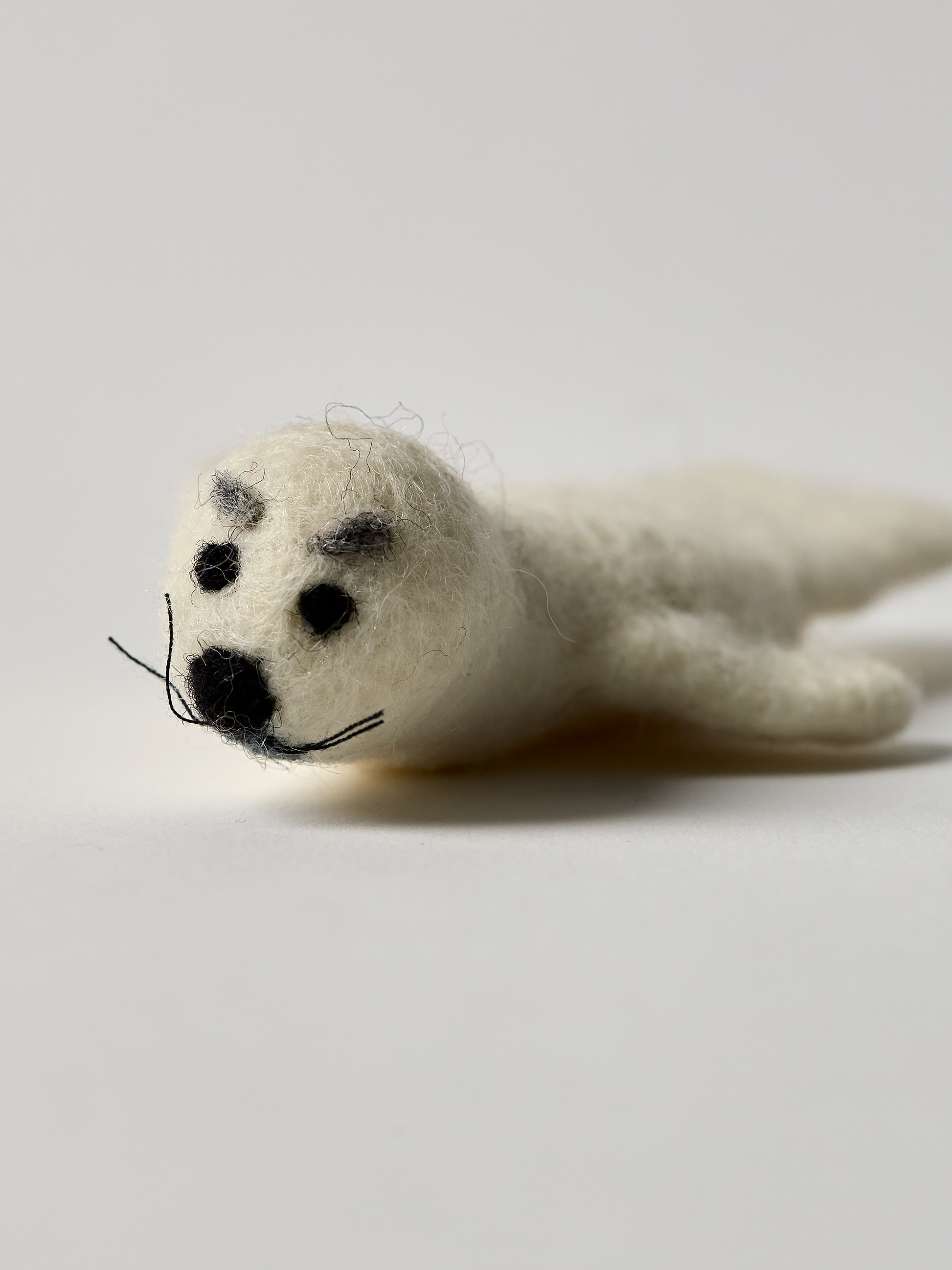 White seal finger puppet with black eye brows on a light gray background