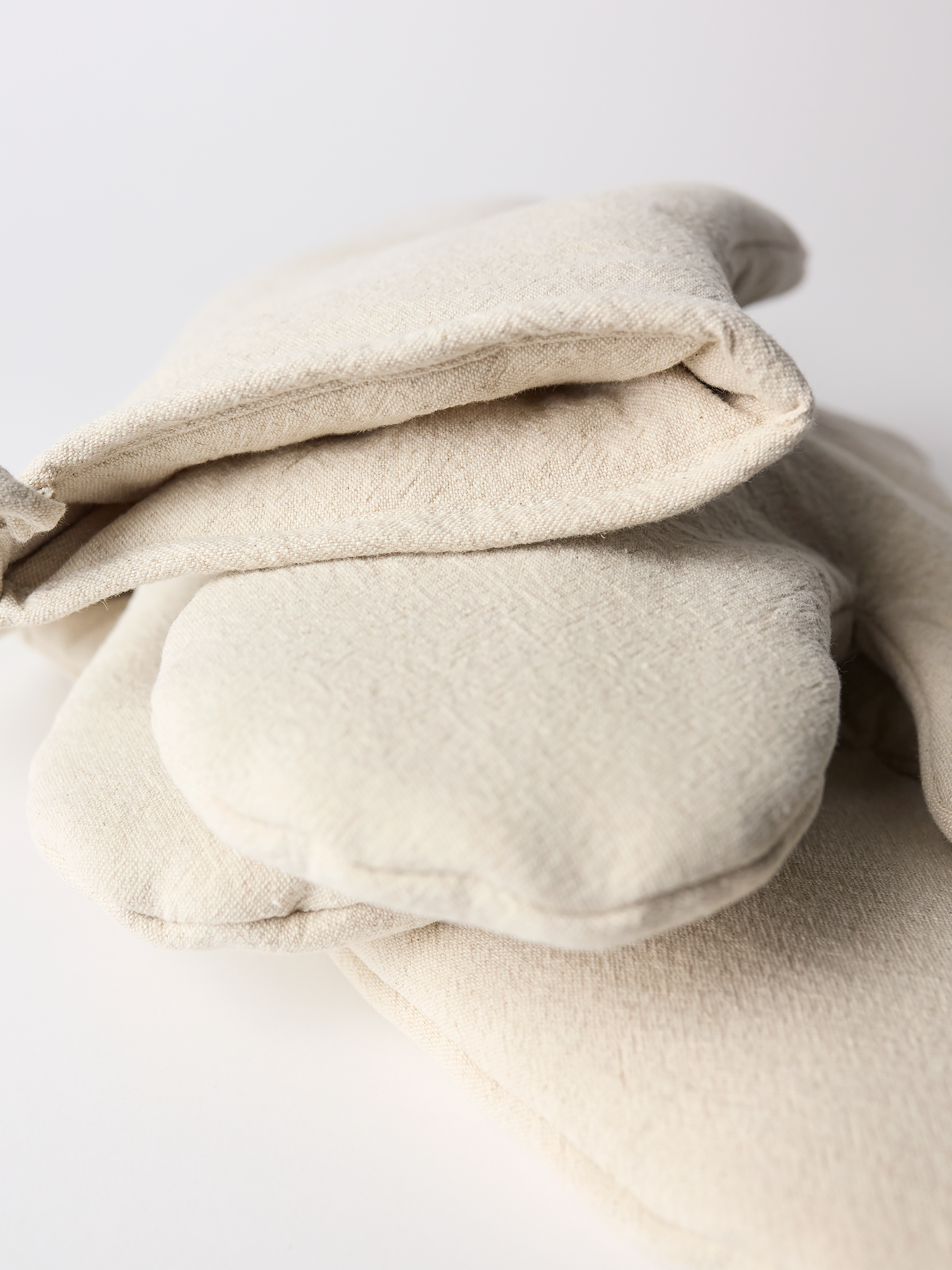 Folded beige oven mitts on a light gray background