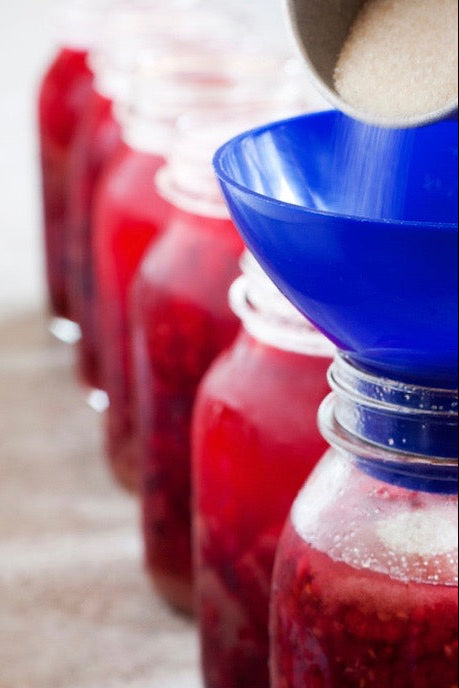 Red jars being filled with a white sugar using blue funnels.