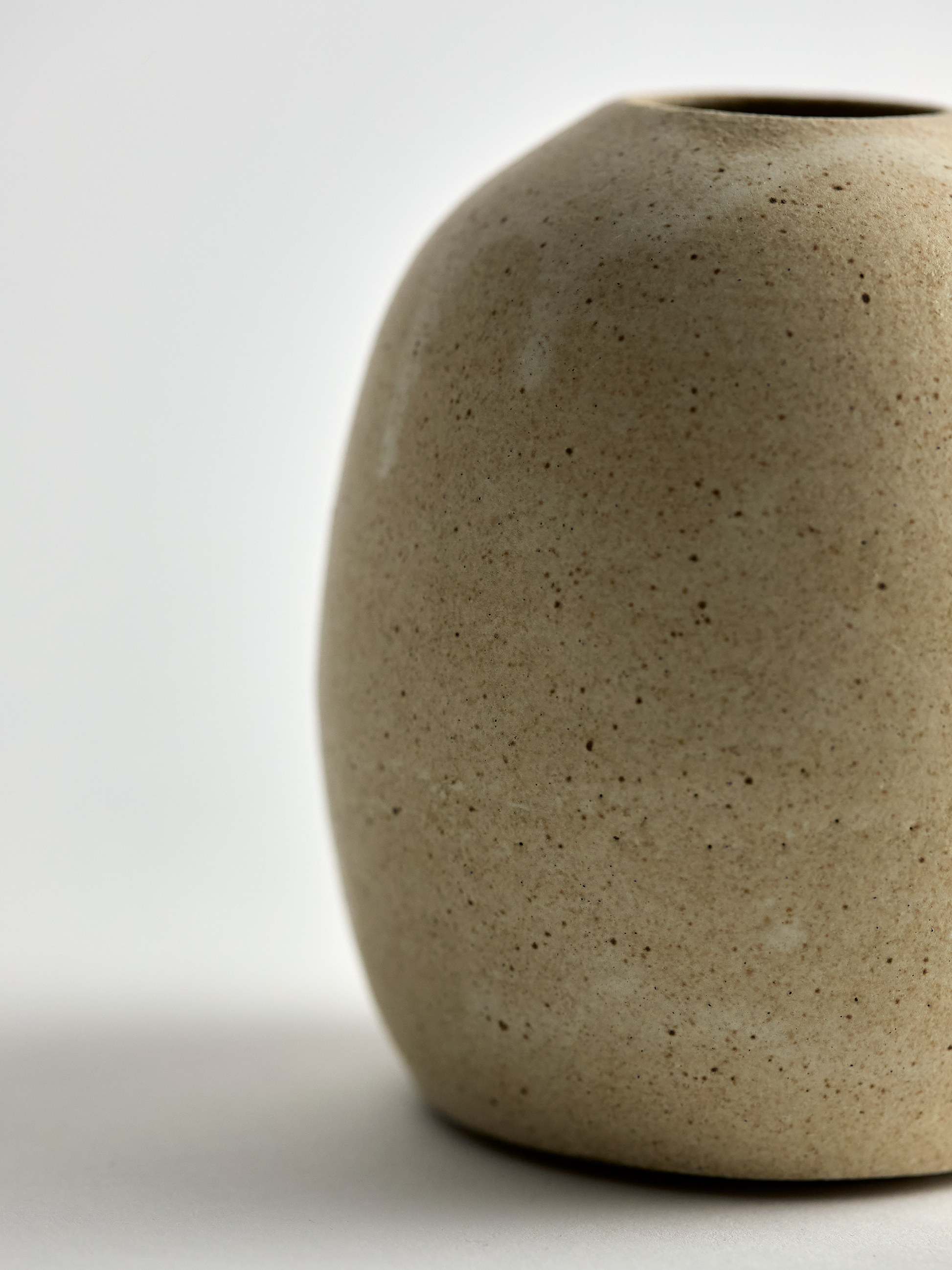 Side view of a textured beige surface  Lorie Stout  ceramic bud vase with on a light gray background