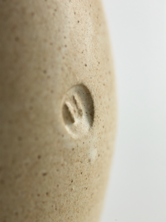 Close-up of a textured ceramic vase with a small circular depression on a light background