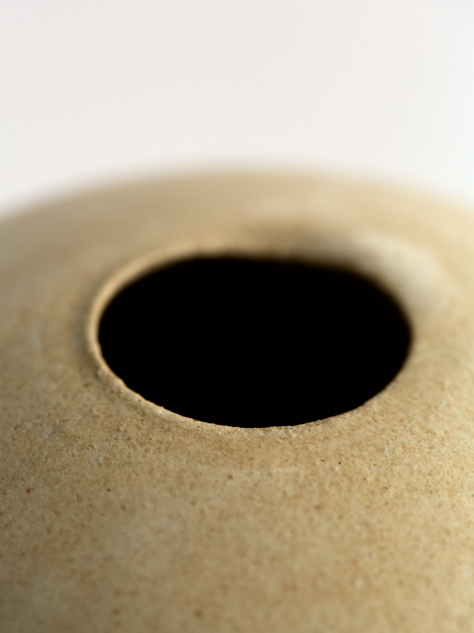 Close-up of a circular hole in a beige surface  Lorie Stout Small  ceramic bud vase with on a light gray background