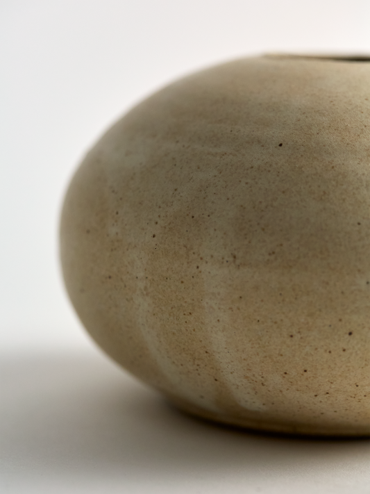 Close up of a Lorie Stout Small beige ceramic bud vase with mark on a light gray background