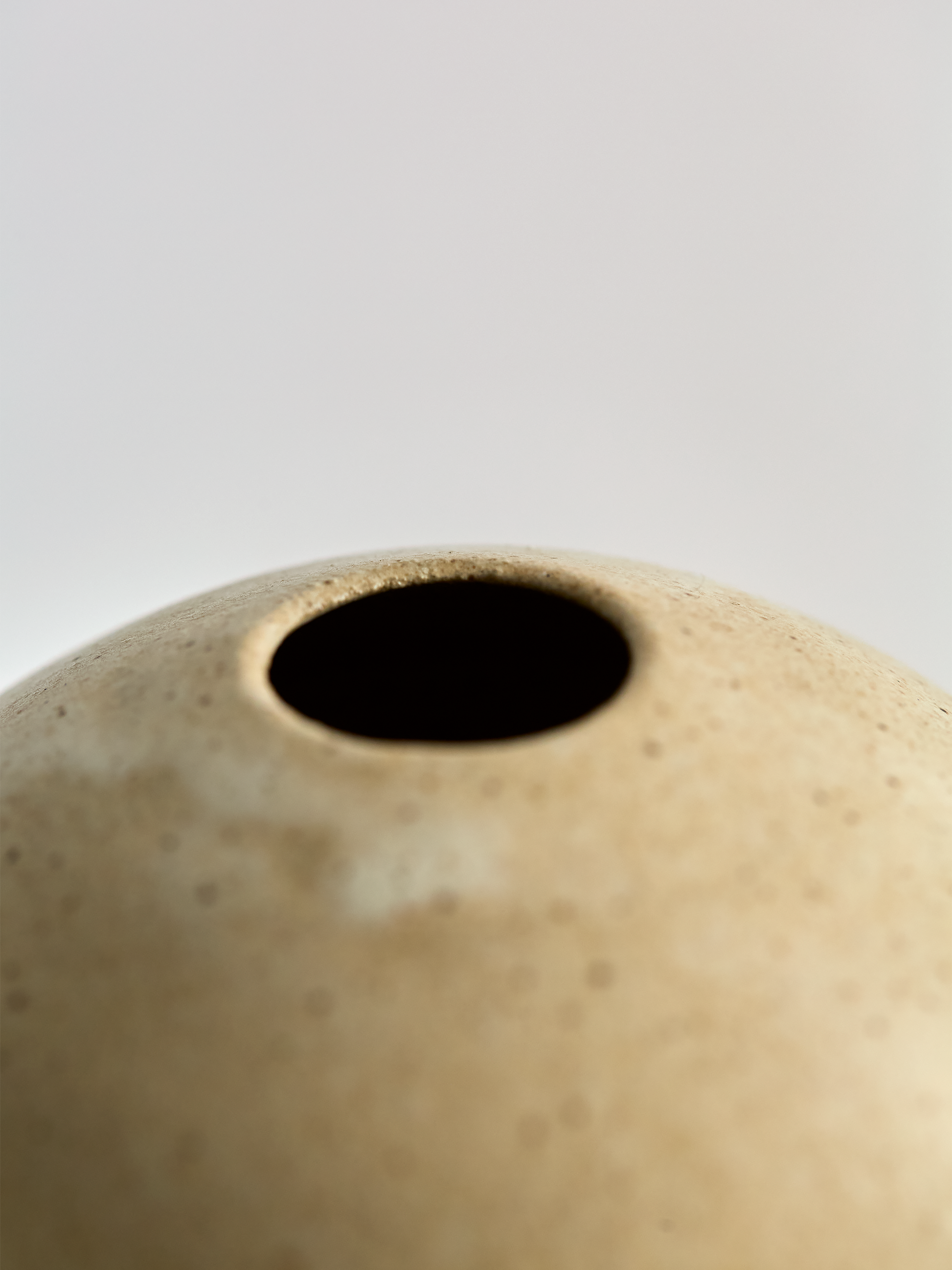Close-up of a Lorie Stout beige ceramic vase with a dark interior on a light gray background