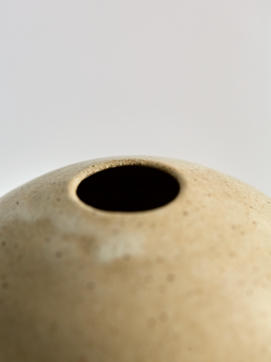 Close-up of a Lorie Stout beige ceramic vase with a dark interior on a light gray background
