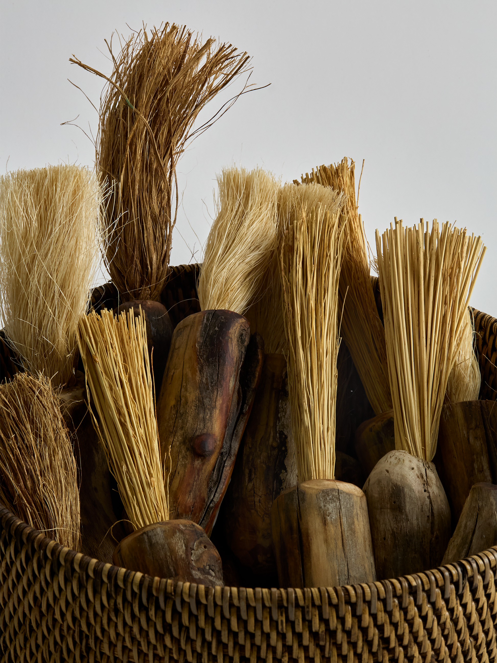 Collection of wooden brushes with various bristles in a woven basket against a neutral background