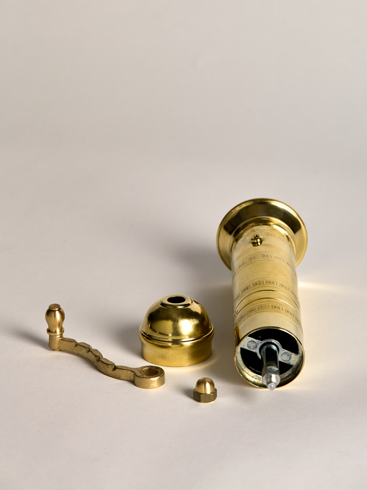 Brass pepper grinder parts on a beige background