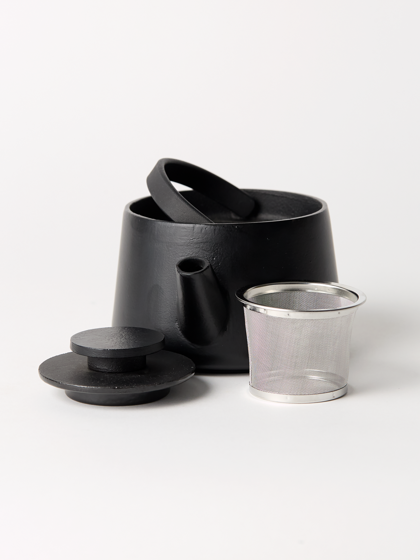 Black ceramic teapot with wire filter on a white background