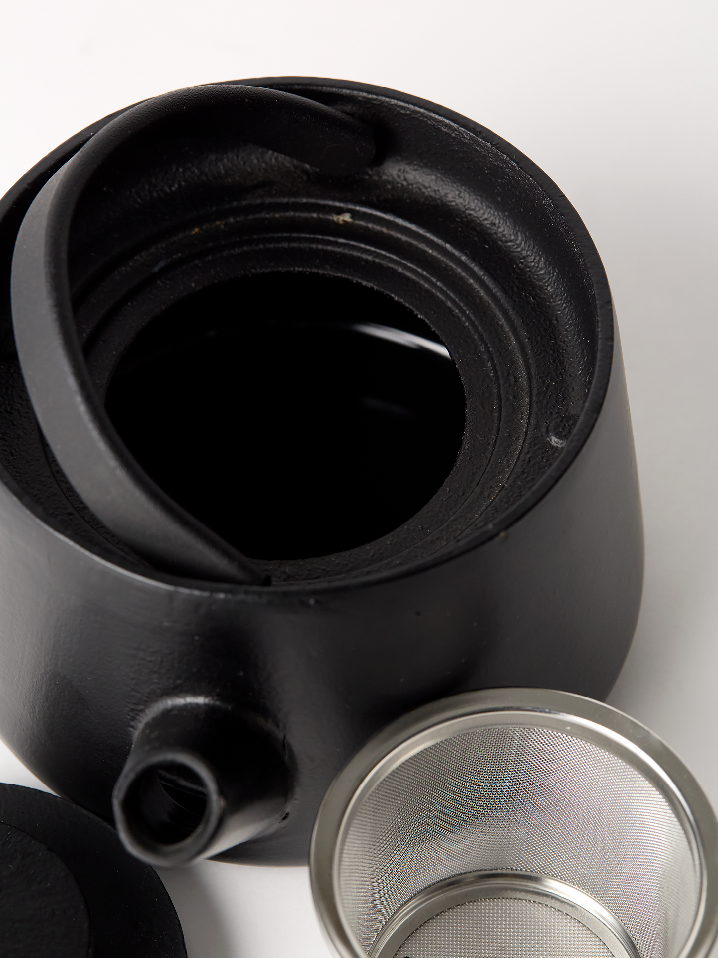Black ceramic teapot with a metal filter on a white background