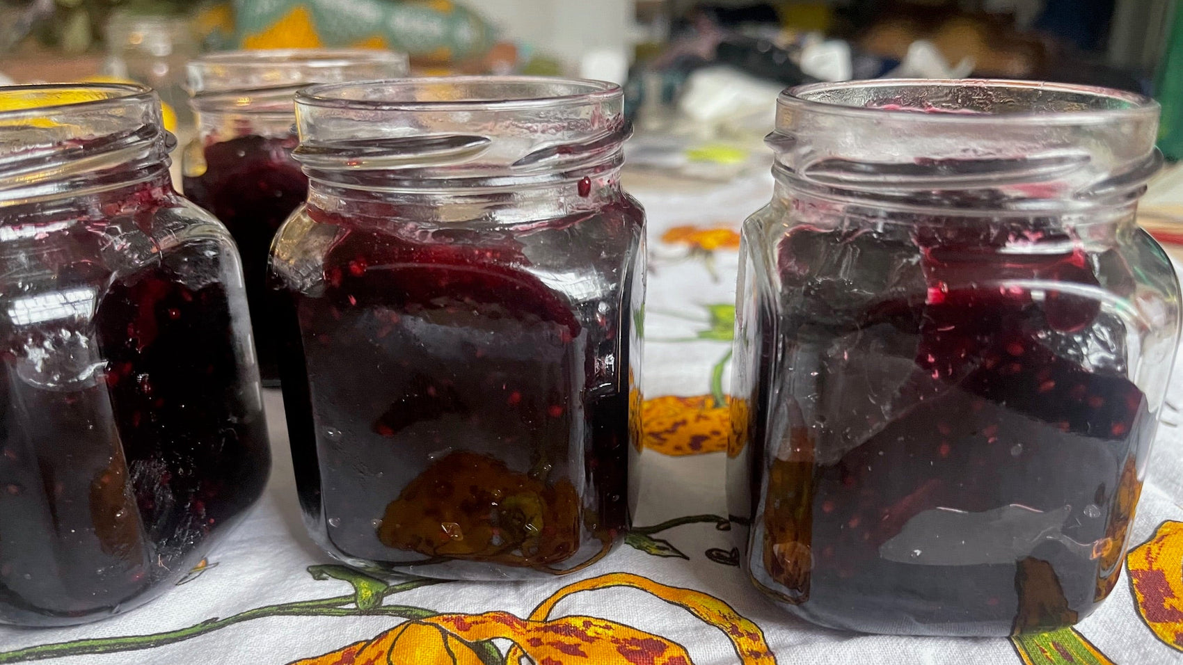 Three glass jars with berry preserves on a floral tablecloth