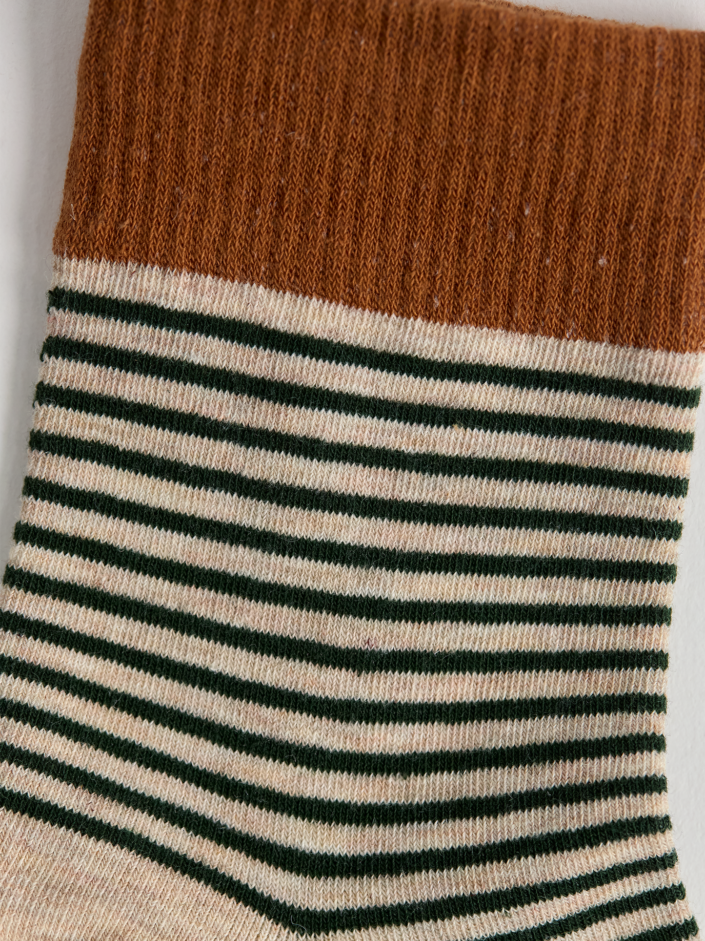 Close-up of striped sock with brown top and green and white stripes on a light gray background.