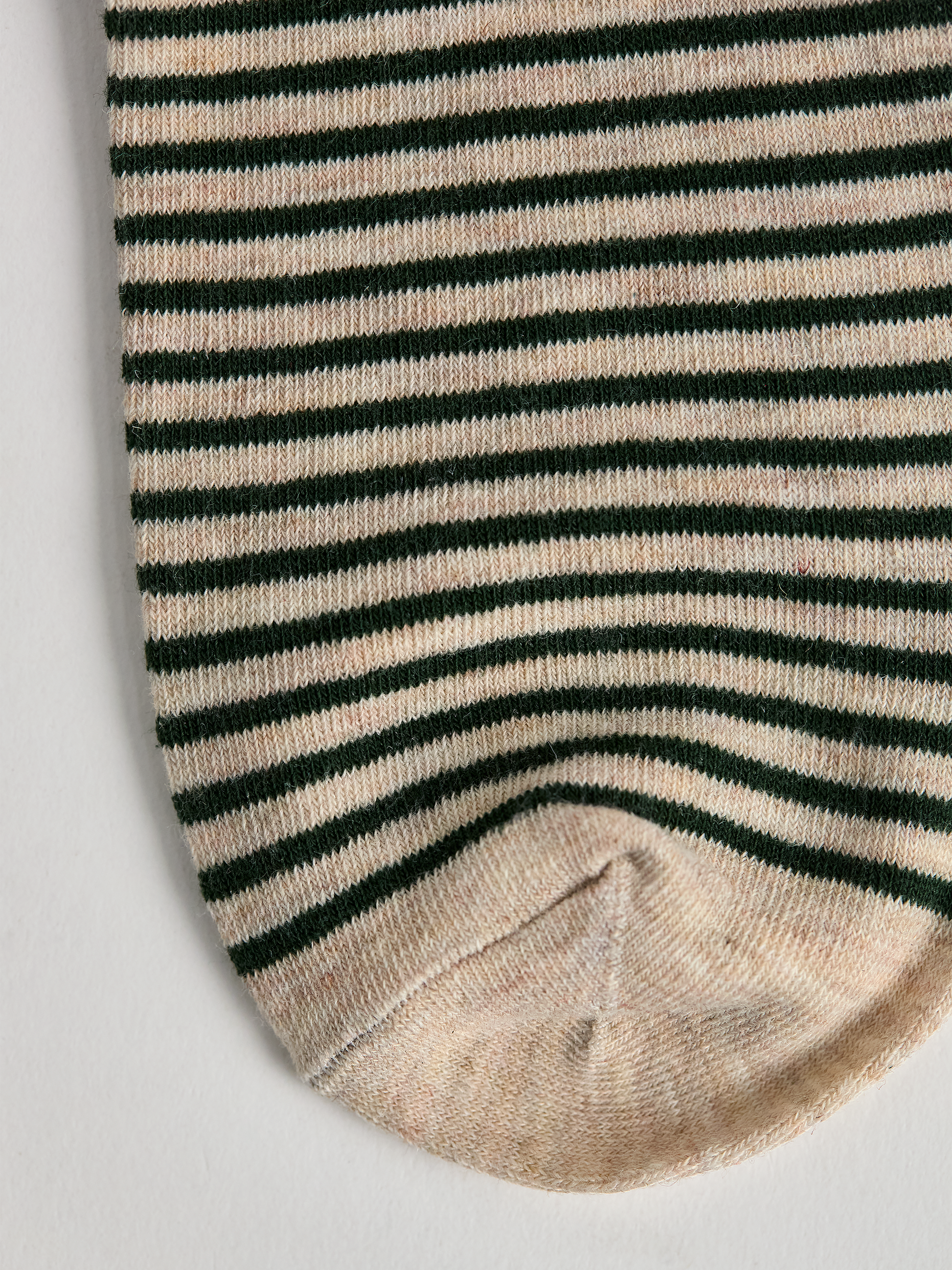 Close-up of striped sock toe with green and white stripes on a light gray background.