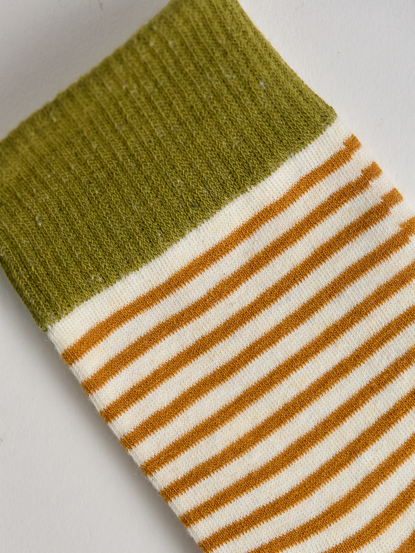 Close-up of striped sock with green top and gold and white stripes on a light gray background.