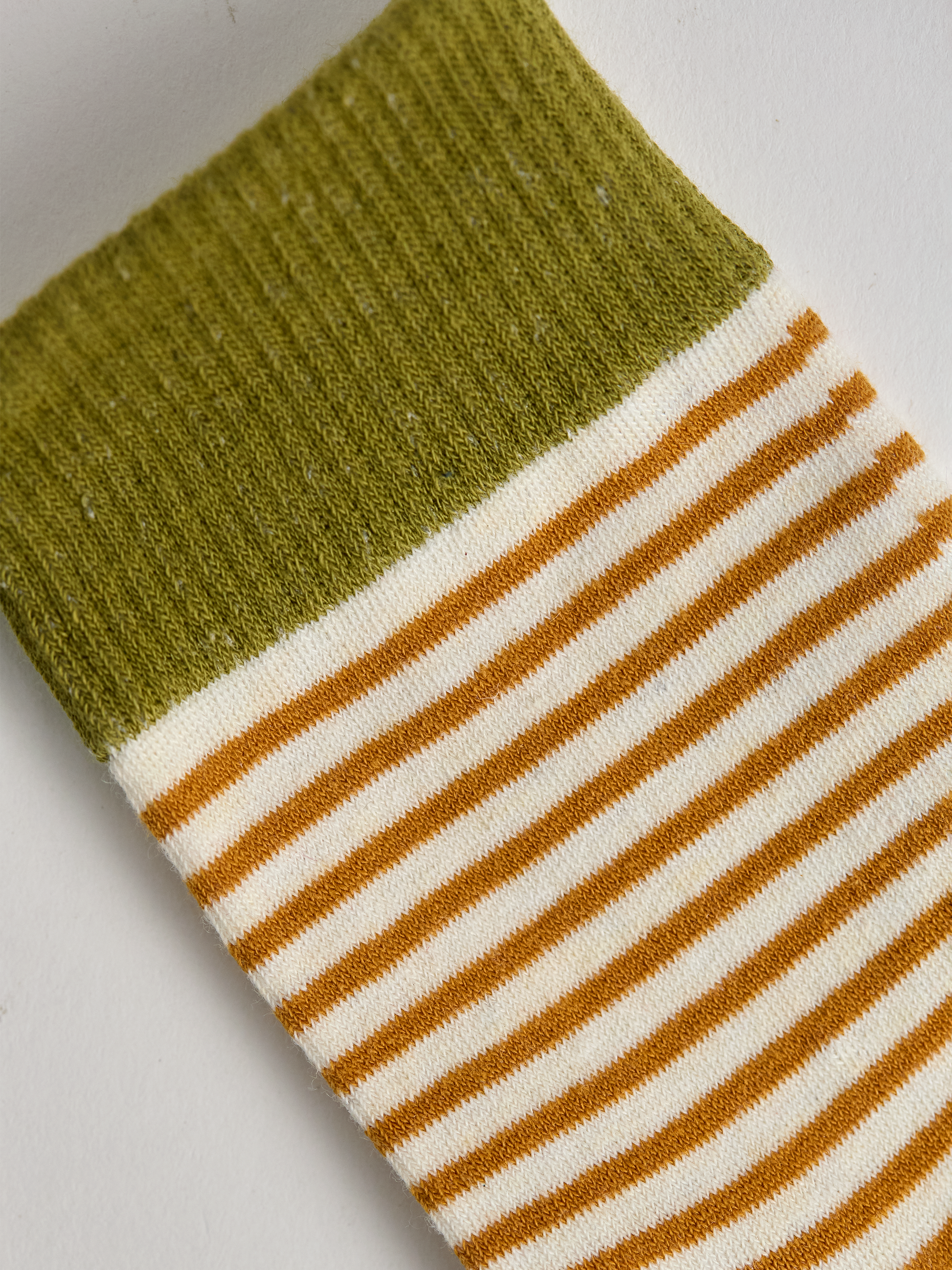 Close-up of striped sock with green top and gold and white stripes on a light gray background.