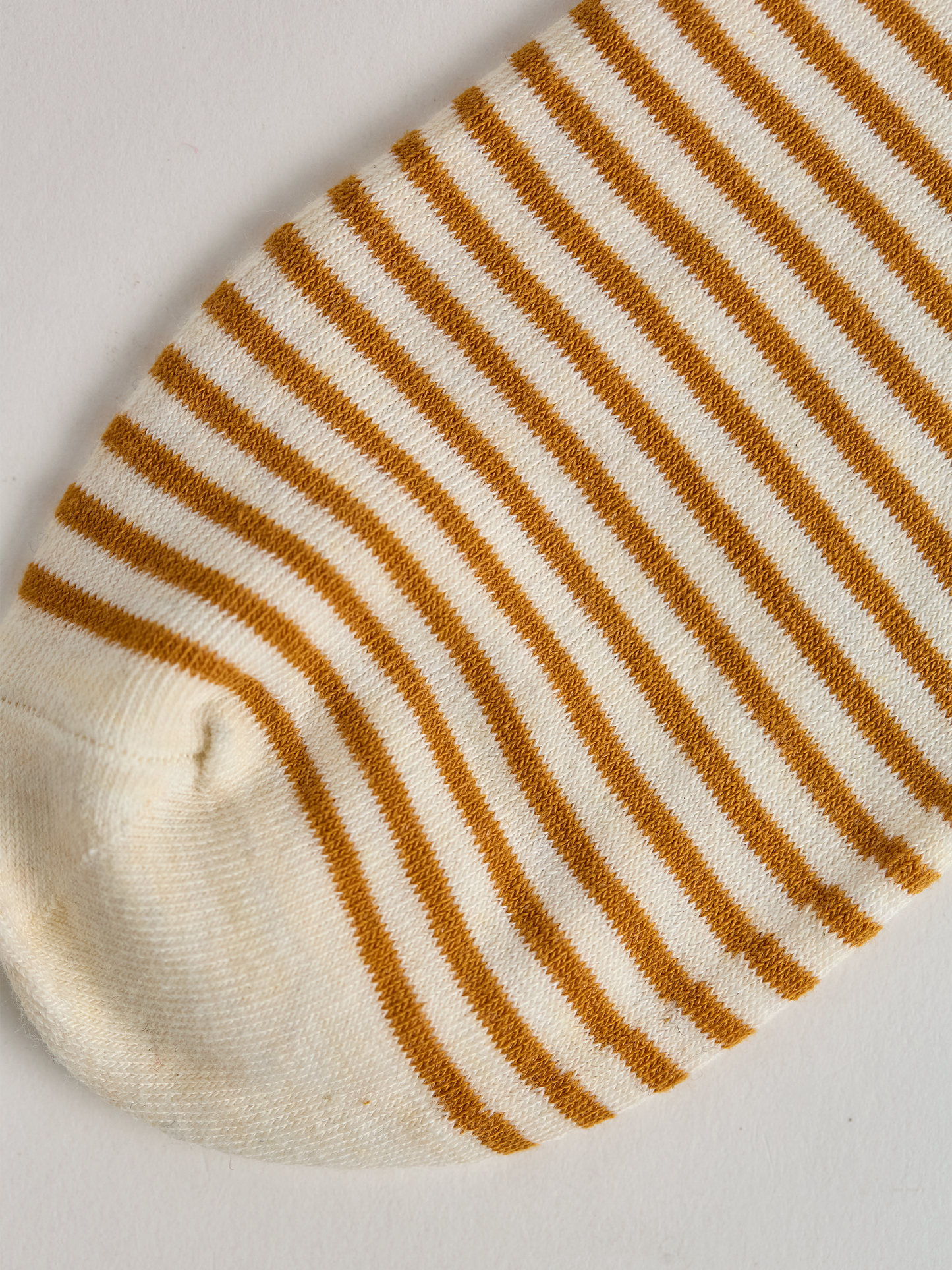 Close-up of striped sock toe with gold and white stripes on a light gray background.