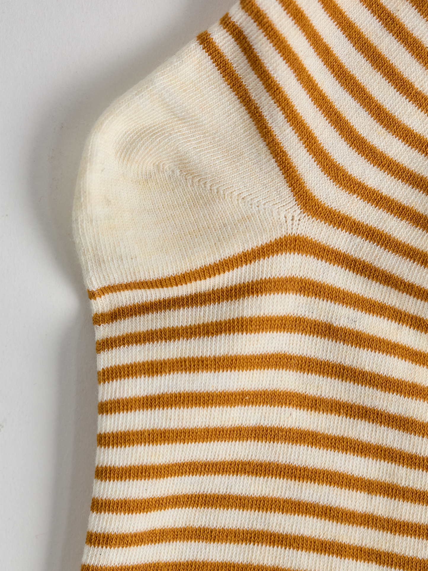 Close-up of striped sock heel with gold and white stripes on a light gray background.