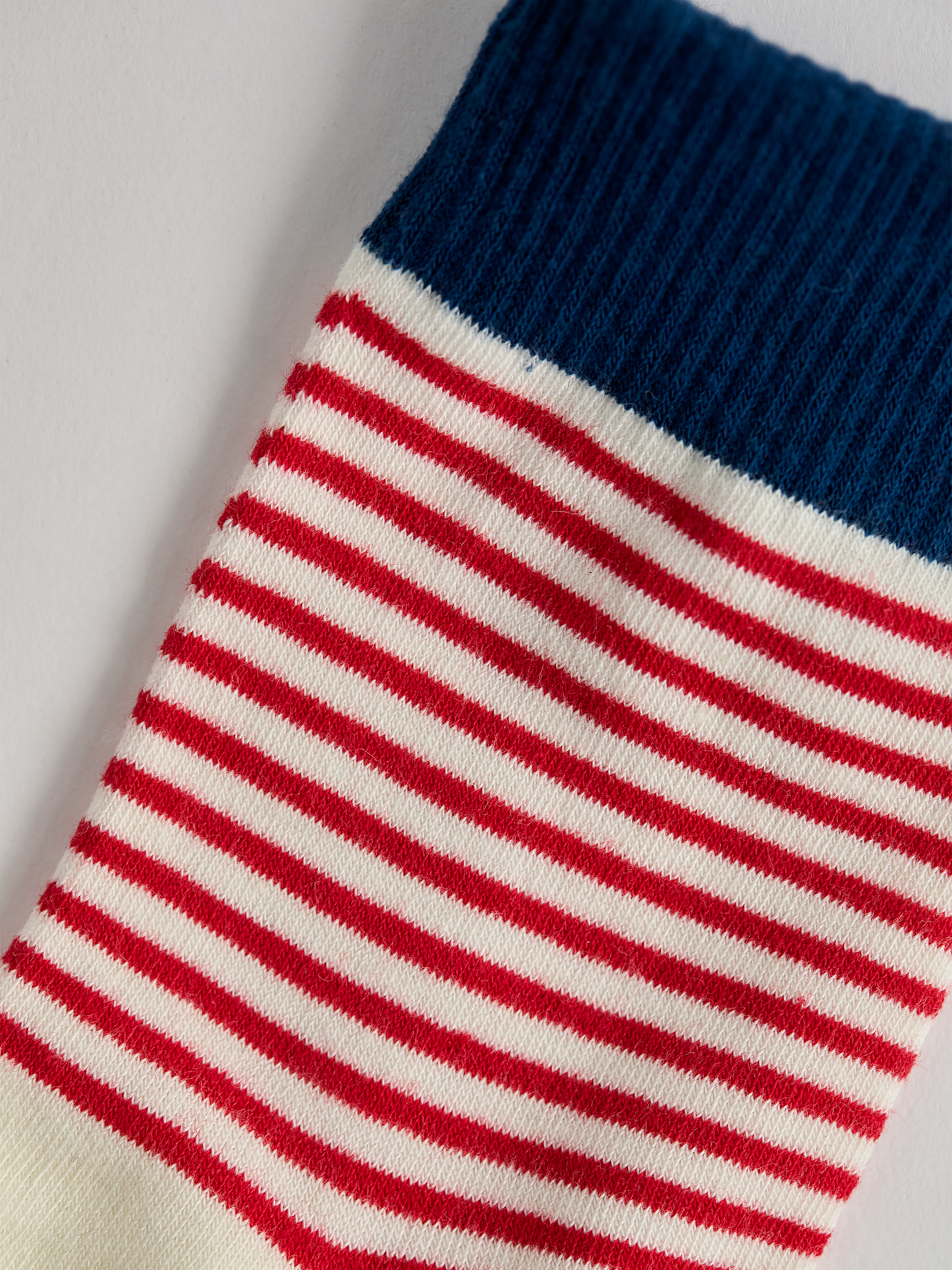 Close-up of striped sock with blue top and red and white stripes on a light gray background.