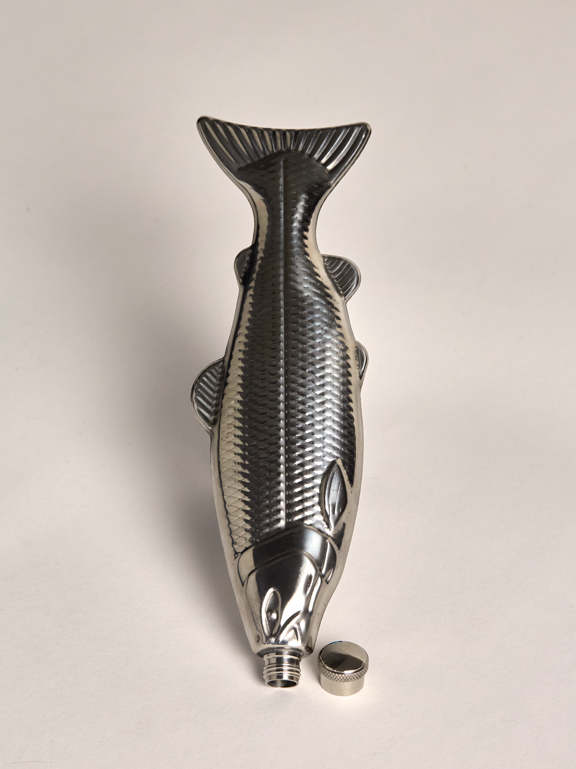 Fish-shaped metal flask on a light gray background with cap off