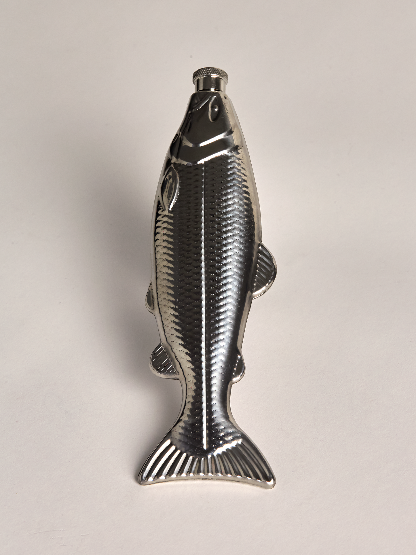 Metallic fish-shaped flask on a light gray background