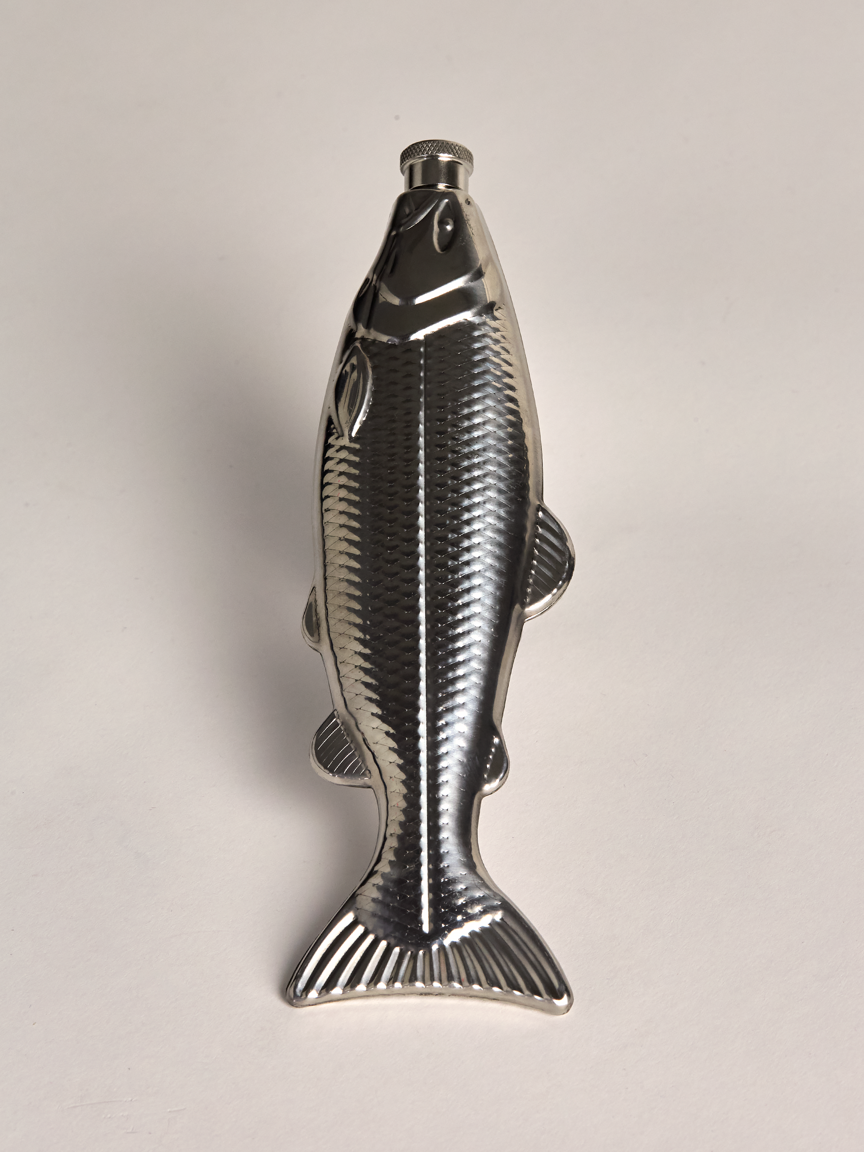 Metallic fish-shaped flask on a light gray background