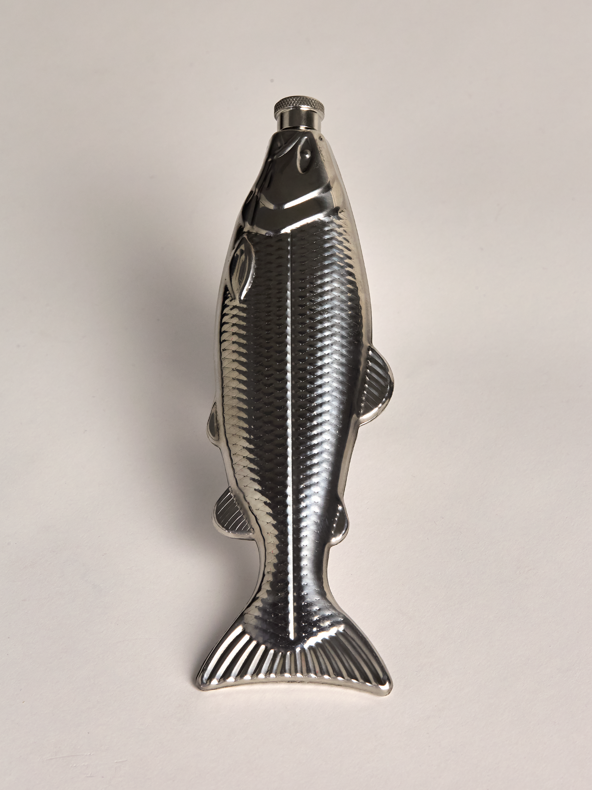 Metallic fish-shaped flask on a light gray background