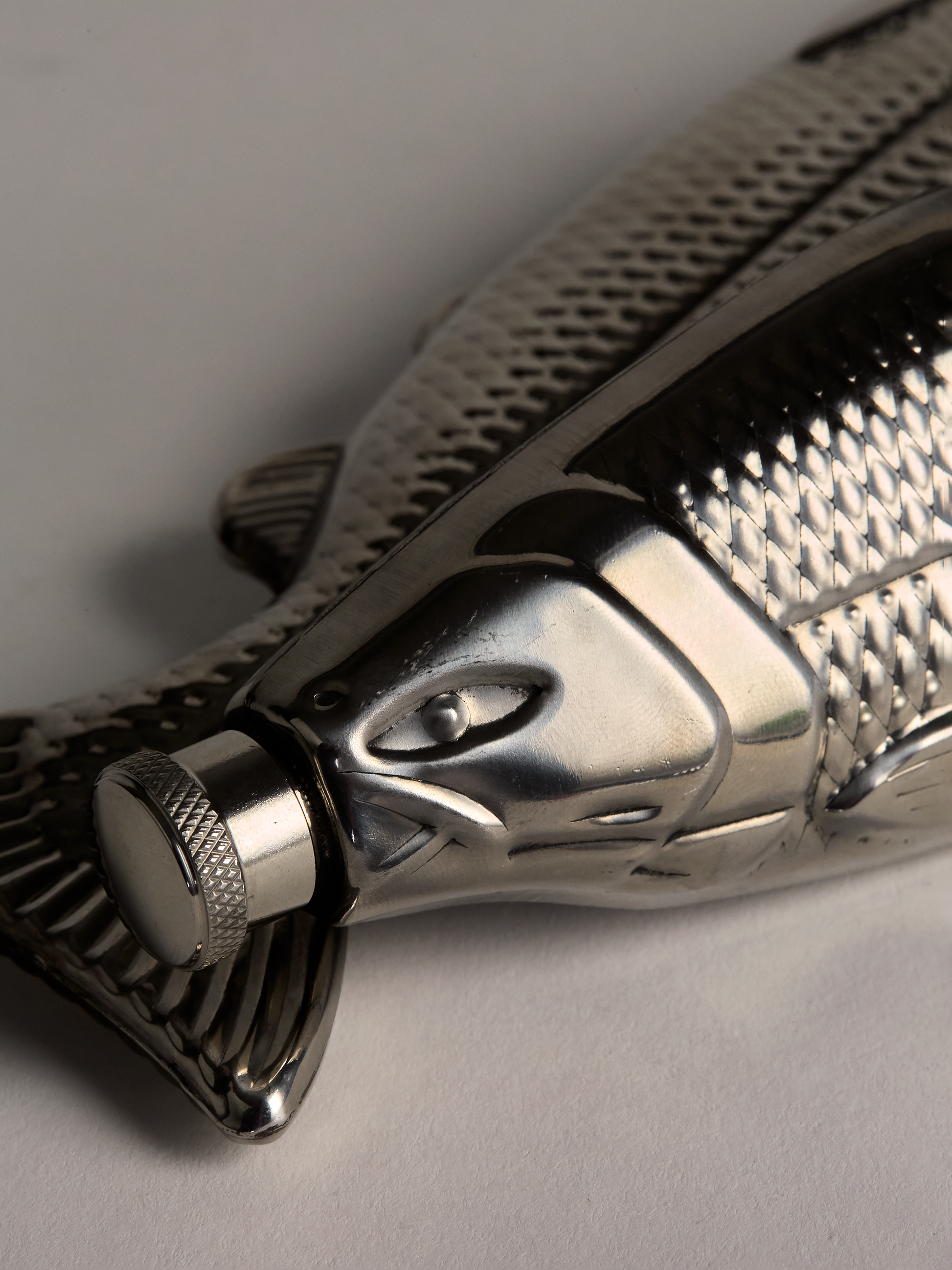 Close-up of a Metallic fish-shaped flask on a gray background